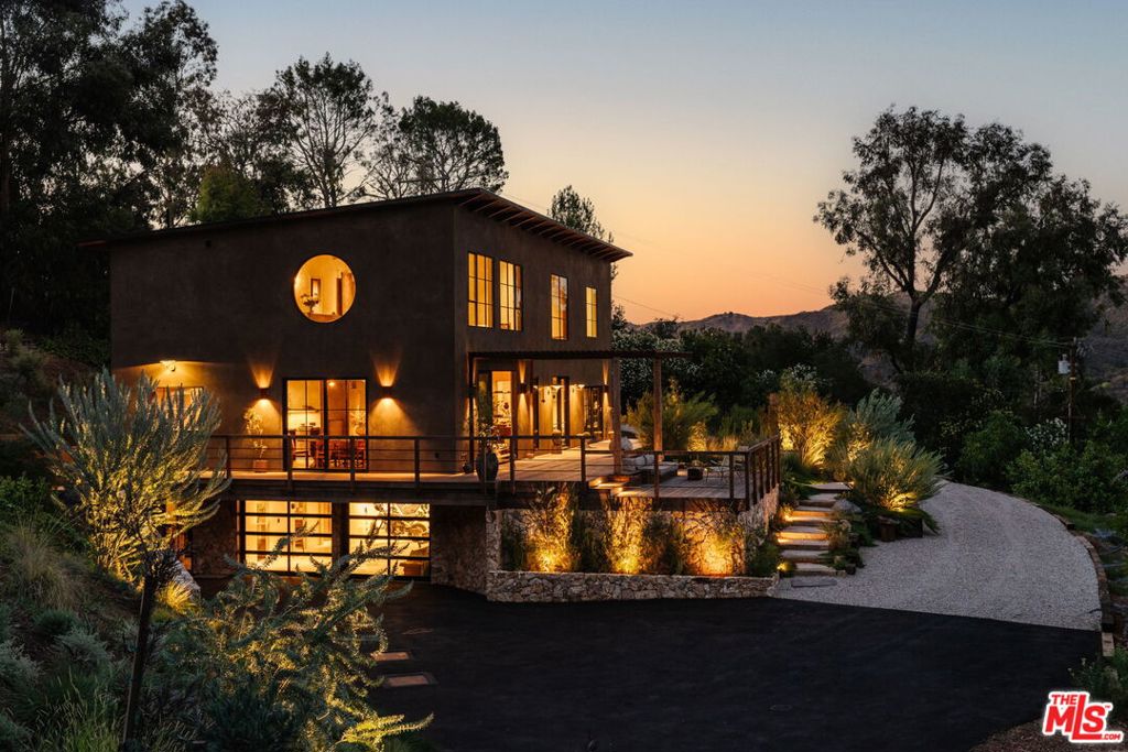 Rascal Ranch: A Masterpiece of Craftsmanship and Design. Nestled along Topanga's most coveted road, Rascal Ranch epitomizes refined craftsmanship and innovative design. This expansive estate offers unparalleled privacy and sweeping, unobstructed canyon views, harmoniously blending modern elegance with the serene beauty of its natural surroundings.The open-concept interior features hand-troweled plaster walls that showcase the shifting light, paired with micro-cement flooring which exudes warmth and sophistication. Expansive doors open to decks and lush gardens, creating an effortless flow for entertaining and tranquil living. At the heart of the home, the kitchen's bandsawn walnut cabinetry, raw leathered quartzite, and Ceppo marble countertops are complemented by state-of-the-art appliancesa striking fusion of form and function.A custom steel and walnut staircase ascends to the second floor, where a floating cork light sculpture and verdant canyon vistas captivate the eye. Wide-plank antique oak floors lend warmth, enhanced by bespoke walnut window sills, door frames, bookshelves, and millwork. Each of the 4.5 bathrooms is a masterpiece, with organic stonework and basins that double as art.The partially subterranean lower level offers a two-car garage, laundry, full bath, and a versatile interpretive space. Fully self-sufficient, Rascal Ranch draws water from two deep wells (150 and 350 feet) and is crowned with a newly installed, 30-year fire-resistant roof. The meticulously designed landscape integrates native California and Australian flora, supported by advanced irrigation and lighting systems. A private orchard, brimming with mature fruit and olive trees, completes this seamless union of home and nature.