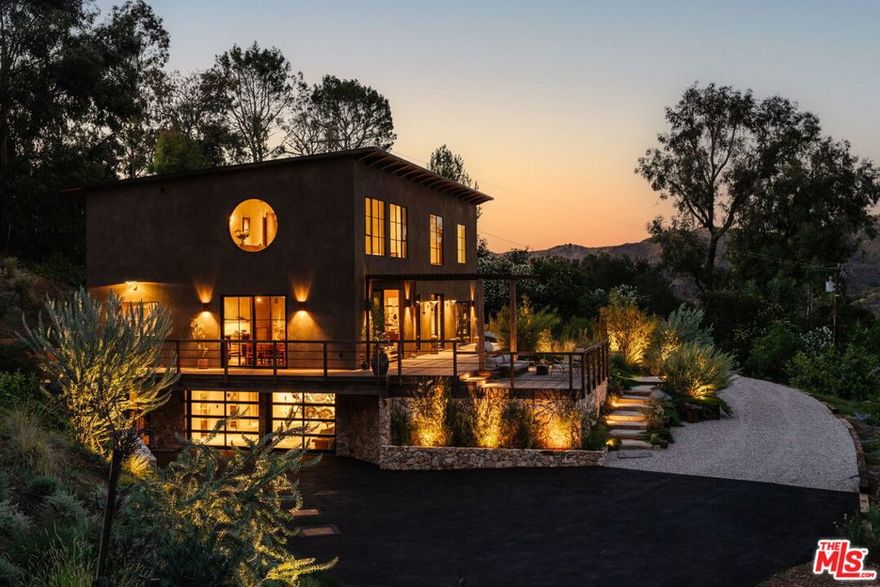 Rascal Ranch: A Masterpiece of Craftsmanship and Design. Nestled along Topanga's most coveted road, Rascal Ranch epitomizes refined craftsmanship and innovative design. This expansive estate offers unparalleled privacy and sweeping, unobstructed canyon views, harmoniously blending modern elegance with the serene beauty of its natural surroundings.The open-concept interior features hand-troweled plaster walls that showcase the shifting light, paired with micro-cement flooring which exudes warmth and sophistication. Expansive doors open to decks and lush gardens, creating an effortless flow for entertaining and tranquil living. At the heart of the home, the kitchen's bandsawn walnut cabinetry, raw leathered quartzite, and Ceppo marble countertops are complemented by state-of-the-art appliancesa striking fusion of form and function.A custom steel and walnut staircase ascends to the second floor, where a floating cork light sculpture and verdant canyon vistas captivate the eye. Wide-plank antique oak floors lend warmth, enhanced by bespoke walnut window sills, door frames, bookshelves, and millwork. Each of the 4.5 bathrooms is a masterpiece, with organic stonework and basins that double as art.The partially subterranean lower level offers a two-car garage, laundry, full bath, and a versatile interpretive space. Fully self-sufficient, Rascal Ranch draws water from two deep wells (150 and 350 feet) and is crowned with a newly installed, 30-year fire-resistant roof. The meticulously designed landscape integrates native California and Australian flora, supported by advanced irrigation and lighting systems. A private orchard, brimming with mature fruit and olive trees, completes this seamless union of home and nature.