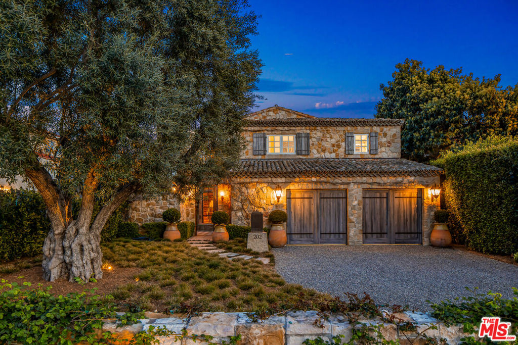 A Samuel Yellin-designed wrought iron gate, together with an expanse of French Bourgogne limestone and potted topiaries, give this Santa Monica residence the feel of a wine country escape. Reclaimed roof tiles from Burgundy, terra-cotta flooring, an antique horse trough and iron-and-glass doors complete the light-filled entryway to the meticulously designed house set on an expansive lot along palm-lined Georgina Avenue. Garage-concealing coach doors that open outward, hand-shaped window shutters and reclaimed beams throughout the house establish a neutral palette of natural materials. Climbing wisteria blooms add a touch of color. Terra-cotta tiles on the enclosed front courtyard lead to a glass-and-metal front door created by Architectural Iron Works artisans in San Luis Obispo. The house's outdoor earthy hues are mirrored by interiors with walls made entirely of plaster, adding softness and dimension. A seamless curving staircase establishes the space's clean, artistic lines. French white oak floors throughout the two-level residence are smoked rather than stained, revealing an embrace of modern restraint. Living room doors open to a spa deck and an Uzes pottery-lined pool, while a library, complete with a gas fireplace and Ingo Maurer lighting is situated above the house's underground wine cellar, visible through a window in the floor. The temperature-controlled cellar, with minimalist shelving made of African walnut, has French limestone flooring and connects to a stone staircase. The light-filled open kitchen with a Roman brick wall includes an island with a Spekva wooden countertop from Denmark, a copper-and-white La Cornue range and hood with electric and gas ovens, and an indoor pizza oven leading to an alfresco outdoor dining area and Kalamazoo grill atop terra-cotta tiles matching those in the living room, all with radiant heat beneath (both indoors and out). A powder room with mother-of-pearl tiles and lighting designed by Venice-based artisans adds a new pale shade to the house's neutral palette. Upstairs, the media room includes a fully-equipped theater with light-minimizing pocket doors and a laser projector plus the hub of the house's electronics including HomeWorks and Savant systems. The residence also has security, complete with cameras surrounding its perimeters and motion-detecting lasers. The theater doubles as an office with a pull-out desk, and is lit with Ingo Maurer flying LED candles. The natural light-filled master bedroom, bordered by a balcony filled with fragrant night-blooming jasmine, includes a custom walk-in closet and overlooks the patio and pool. A spa-like bathroom with a full-size tub plus a shower with steam includes exterior stairs leading to the jacuzzi and pool below. A north-facing guest bedroom, also on the second floor, has an adjoining guest bath with black and white tile and a subtle Greek key print. Hand-painted tiles and plates sourced from San Diego and inspired by Lisbon's blue-and-white azulejos adorn a jacuzzi on the house's back porch. Deep-blue glass tiles line the rectangular pool rimmed with Moroccan lanterns and topiaries in circular Uzes pots. A large one-bedroom guesthouse sits beyond the pool's sun-drenched far corners. Additionally, there is the possibility of creating adjoining exterior space or a second residence through the acquisition of the adjacent property directly to the East of 202 Georgina.