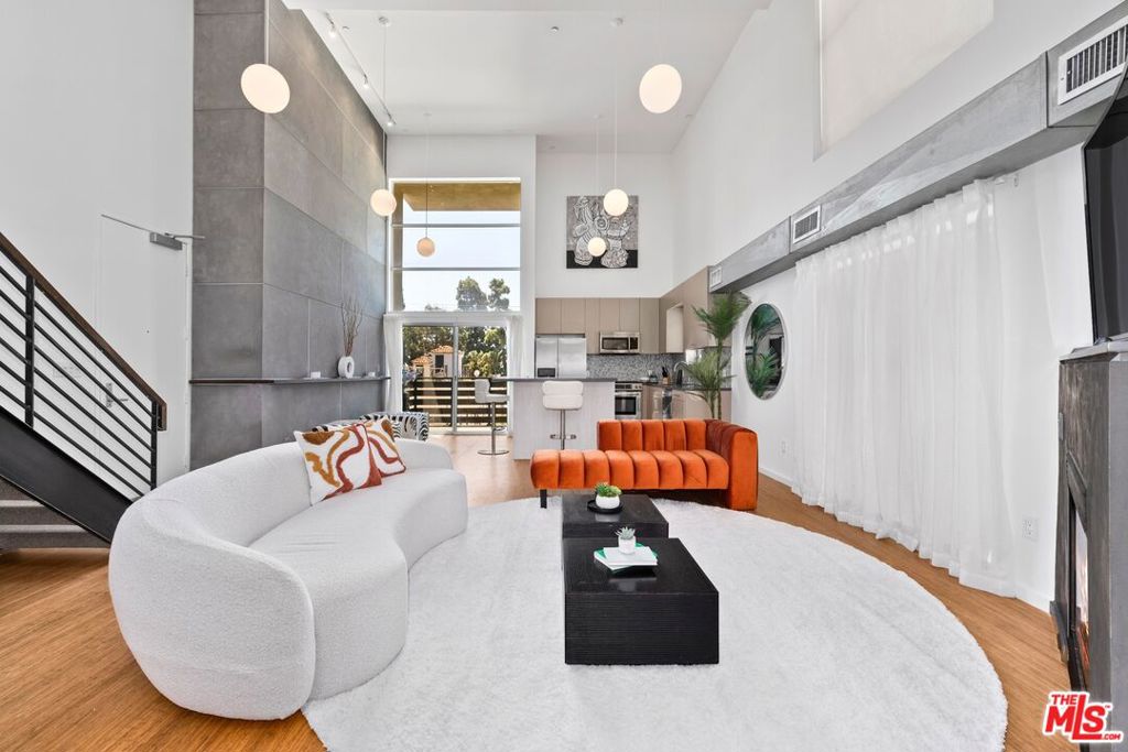 Step into this beautiful, highly functional open loft, where 18-foot soaring ceilings and wall-sized windows flood the space with natural light. Upgraded with a white oak kitchen island, chic Venetian plaster wall and fireplace, sleek glass railings, and a sliding glass wall that transforms the first-floor space into an additional ensuite bedroom-perfect for guests or a home office. The bamboo hardwood floors have also been recently refinished, adding warmth and polish to the modern aesthetic. The streamlined kitchen features Caesarstone countertops and mosaic tile accents, continuing the elevated design into both the kitchen and bathrooms. Additional features include a private balcony, in-unit laundry, two gated tandem parking spaces, dramatic architectural hallways, a contemporary water feature entry, and nine guest parking spots- rare perks in the city. Located in the heart of Hollywood, just minutes from the Roosevelt Hotel, Runyon Canyon, and The Venue of Hollywood, this loft places you at the center of it all. The building's community rooftop deck is equally impressive, offering panoramic views of the Hollywood Hills, breathtaking sunsets, and the iconic Hollywood Sign. It's the perfect place to soak in the city's energy. This is true LA living: style, flexibility, and a front-row seat to Hollywood's vibrant lifestyle.