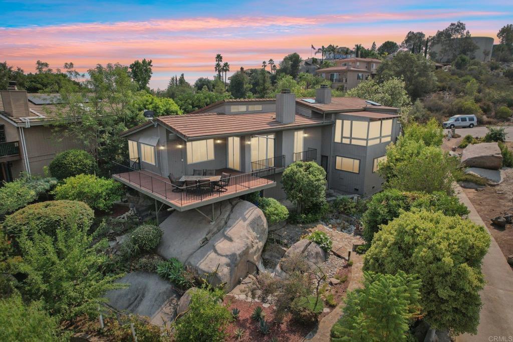 Perched at the top of a quiet cul-de-sac, this unique home is built right into the hillside, surrounded by incredible giant boulders—one even greets you just inside the front door! Enjoy sweeping mountain views from the open living spaces and the oversized deck, perfect for soaking in the peaceful setting. Inside, each of the three bedrooms has its own bathroom. The entry-level bedroom is oversized for flexible use with no stairs, while the primary suite features a bonus sitting area, private deck access, fireplace, and a spa-like bathroom with double sinks, a large closet, and a relaxing jacuzzi tub. The third bedroom also captures the mountain views and can serve multiple purposes either open or enclosed. The open kitchen offers granite countertops, stainless steel appliances, and flows seamlessly into the living area. Recent upgrades include a Brand New heating and air conditioning system (2022), five new skylights (2023), and motorized solar-shade blinds. The outdoor spaces are just as special—peaceful garden pathways lead to fruit trees (lemon, lime, tangerine and plum) plus two blackberry bushes. There’s abundant parking, RV space, and a finished garage to round out the property. A home like this—where nature and comfort meet—is truly one of a kind.
