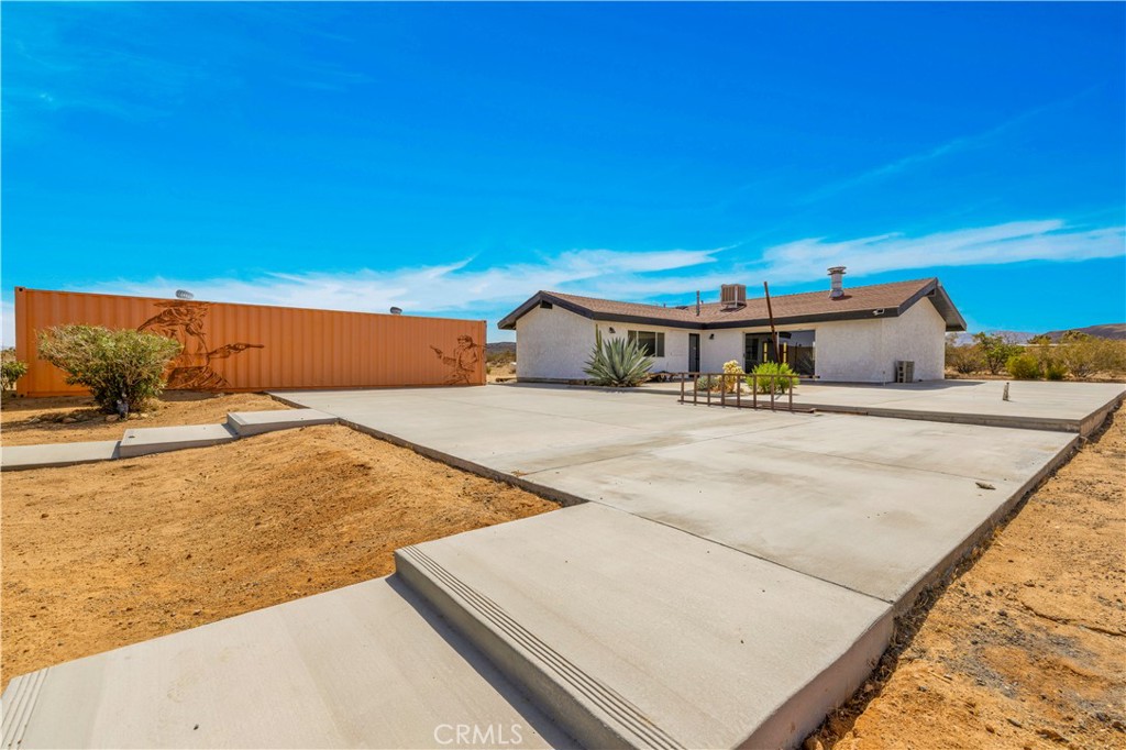Set on 9 acres across two parcels, this desert retreat offers the rare combination of privacy and convenience. Just minutes from town yet surrounded by wide-open views, the property delivers space to breathe and create. The main home features 2 bedrooms, 1 bathroom, soaring wood-beam ceilings, polished concrete floors, and an open living area centered around a striking freestanding fireplace. The kitchen blends rustic charm with modern function, offering generous counter space, open shelving, and warm cabinetry.
Recent updates include three new mini split systems for efficient climate control and leased solar to help offset energy costs. Outdoors, the property showcases extensive concrete work surrounding the home, ideal for adding a workshop, sport court, or even a pickleball court. A circular patio with a built-in shade structure provides the perfect place to enjoy panoramic desert and mountain views.
The second 5-acre parcel includes a small cabin with water and power, offering additional potential for restoration or creative use (buyer to verify with county). A mural-accented storage container adds further versatility as storage or creative space.