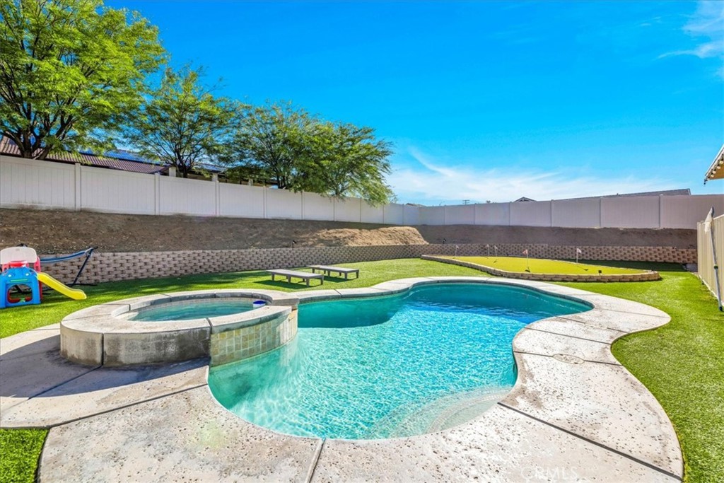 Welcome to 56135 Nez Perce, a stunning turn-key POOL home located in the highly desirable Mesquite neighborhood of Yucca Valley. This beautifully maintained 3 bedroom, 2 bath property is nicely situated on a large corner lot and features 1,764 square feet of living space. As you step inside the bright & airy great room you'll find 10-foot ceilings, earth-toned tile flooring, a lovely gas fireplace and large windows that let in an abundance of natural light. This home's modern style and open-concept layout is one to be desired. The living room flows effortlessly into the dining and kitchen area complete with recessed lighting, upgraded appliances, a center island with beautiful granite countertops and bar seating, ample cabinet & counter space and a walk-in pantry. All bedrooms have carpeted floors & ceiling fans, and the primary bedroom adorns french doors and a sliding glass door that leads to the back patio. The ensuite bathroom is sure to impress with a dual sink vanity, jetted tub, walk-in shower and huge walk-in closet. There is also a convenient indoor laundry room just off the kitchen with a utility sink and additional cabinetry for storage. That's just the inside! The backyard is truly an entertainer's paradise. From the awe-inspiring in-ground pool and spa to the turf putting green, large covered patio with ceiling fans, stucco pergola, Vinyl privacy fencing and ample space for BBQs and get togethers, it's like having a little resort right outside your back door. Not to mention the oversized 3 car garage, low HOA and close proximity to town, schools, shopping, eateries & more! Come take a look & let this homes charming allure do the rest, your new desert home or weekend retreat awaits!
