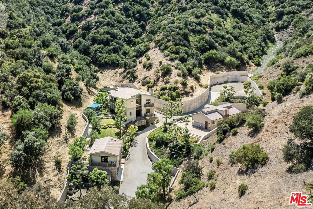 Tucked away at the very end of coveted Mandeville Canyon, Stone Hollow is a breathtaking 7.5-acre estate where timeless rustic charm meets refined California living. Offering total privacy, generous scale, and striking natural beauty, this one-of-a-kind compound features a 5-bedroom, 5-bathroom main residence with over 5,400 sq ft of thoughtfully designed living space plus a detached 700 sq ft guesthouse above a 3-car garage. A secure gated entrance opens to a long, private drive that winds past mature trees and lush landscaping. The main home, built in 2006, radiates warmth and understated sophistication, with natural stone finishes, vaulted wood-beamed ceilings, rich textures, and expansive views of the surrounding canyon. Walls of glass and open, airy living spaces create seamless indoor-outdoor flow throughout. The layout is ideal for entertaining and everyday living, with a chef's kitchen, formal and informal dining areas, and a dramatic living room anchored by a statement fireplace and large picture windows. Outside, expansive flat lawns, stone patios, a tucked-away spa, fire pit lounge, multiple seating areas invite relaxing outdoor living year-round. Meandering pathways and manicured gardens further enhance the sense of retreat. Just beyond the residence is a professional-grade equestrian facility, complete with a 4-stall barn, tack room, wash area, gym, and a riding arena. While no longer an active ranch, the infrastructure remains intact offering endless possibilities for horse lovers, creative reimagining, or simply enjoying the space and flexibility it provides. Minutes from the heart of Brentwood, yet a world away, Stone Hollow is a true legacy property rarely available and impossible to replicate. For those seeking nature, serenity, and luxurious space without leaving Los Angeles, there is nothing else like it.
