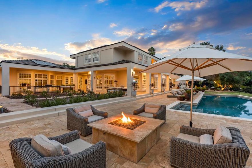 Behind private gates in the heart of the Rancho Santa Fe Covenant, this timeless estate offers the perfect blend of sophistication, comfort, and resort-style living on two pristine acres. With 7,717 square feet of living space, the property encompasses a 5-bedroom, 5.5-bath main residence and a detached 1bed/1bath guest casita, surrounded by lush landscaping and expansive grounds designed for both privacy and entertaining.  Inside, the home’s modern traditional design combines classic craftsmanship with warm, inviting spaces. Soaring ceilings and an open floor plan create a natural flow, while large-scale windows and French doors frame garden views and bring the outdoors in. Formal living and dining spaces are balanced by casual gathering areas, including a game room with a bar, designed for effortless entertaining. The gourmet chef’s kitchen—complete with butler’s pantry, multiple ovens, and a sunny breakfast nook—opens to the family room, where mornings and evenings alike are centered around connection.  The first-floor primary suite commands its own private wing, featuring a sitting area with fireplace, French doors to a covered loggia, dual dressing rooms, and a spa-inspired bath. Upstairs, three additional en-suite bedrooms are joined by generous lounge areas and a bonus room, creating the ideal retreat for family or guests.  Outdoors, the property transforms into a private resort. A sparkling pool and spa are complemented by multiple firepits, a covered outdoor living/dining room, and an outdoor kitchen. Olive trees strung with lights create enchanting spaces to gather, while the greenhouse and gardens offer opportunities for homegrown produce. With wide lawns, fragrant rose gardens, and a serene southern view, every corner of the estate is designed to be enjoyed.  Additional amenities include solar power, garaging for four cars, and direct access to Rancho Santa Fe’s trail system. Just minutes from the Village, golf, tennis, and top-rated schools, this Covenant estate captures the essence of refined living in one of Southern California’s most sought-after communities.