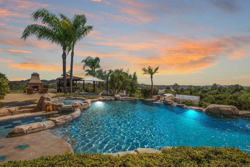 Welcome to Cool Valley Ranch Estates, an exclusive gated community where timeless Mediterranean and Tuscan elegance meets luxurious modern living. Nestled on a spectacular 3.42-acre corner lot, this custom-built, single-story estate offers nearly 4,600 square feet of living space, including 4 spacious bedrooms, 4.5 beautifully appointed baths, and a private guest casita with its own entrance—perfect for multi-generational living or hosting visitors in style.  From the moment you arrive, the striking curb appeal, circular driveway, and lush landscaping with palms, oaks, magnolias, and a butterfly garden set the tone for what awaits inside. Step through the private open-air courtyard with dual solid wood doors and wrought iron accents, and enter a space where light, luxury, and nature harmoniously blend.  Inside, the home showcases a seamless mix of natural materials and high-end finishes, including 18x18 travertine flooring with matching baseboards, solid alder wood doors, Anderson windows and sliders, custom beam ceilings, and soft trowel-finished walls. The heart of the home is the chef’s kitchen—a true culinary masterpiece featuring custom alder cabinetry, slab granite counters, Thermador and Bosch appliances, a pot filler, a warming drawer, an oversized center island, and a spacious walk-in pantry. Just steps away, a butler’s pantry with its own sink, fridge, and lighted cabinets makes entertaining effortless.  Enjoy formal meals in the elegant dining room with sliding doors opening to the courtyard, or cozy up in the library/living room with built-in shelving and serene views. The expansive great room, complete with a wood-burning fireplace and built-in entertainment center, flows effortlessly into the breakfast nook and kitchen, creating an inviting space for gatherings.  Retreat to your luxurious primary suite with its own fireplace and spa-like bathroom with soaking tub, walk-in shower, and custom-organized walk-in closet. There are also two additional ensuite bedrooms, a bonus room (potential fifth bedroom), and a built-in study area. The attached ADU-style casita opens to the courtyard and features a beautifully tiled private bath.  Step outside and discover your private resort. This resort-style, solar-heated saltwater pool features a beach entry, slide, oversized spa, swim-up bar with built-in stools, an underwater swim-through, and two waterfalls—one cascading over a hidden grotto. Entertain year-round under the covered BBQ pavilion, complete with a built-in sink, refrigerator, storage, and bar-top seating for eight. Just beyond, a wood-burning fireplace creates a cozy ambiance between the pavilion and the outdoor living room—a comfortable space connected to the breakfast nook and outfitted with a wall-mounted TV. A pass-through countertop links the outdoor living room to a separate dining area, perfect for enjoying meals al fresco while taking in panoramic western sunsets and, on clear days, glimpses of the Pacific Ocean.  Equestrian enthusiasts will appreciate the 4-stall horse barn, along with a detached tack room that includes two covered stalls equipped with water and electricity, plus a 1-acre turnout area. The property also boasts a 1,050-foot-deep private well with a 5,000-gallon holding tank, 14-stage booster, new pump, and provides full irrigation for the grounds, greenhouse, and gardens.  Additional features include a 13kW solar system with 40 panels, passive pool solar, new spa heater, quad DE pool filter, newer HVAC with 3-zone control, central vacuum, CAT-5 wiring, built-in surround sound, custom built-ins, and a spacious 1,424-square-foot 4-car garage and workshop.  This is more than a home—this is a lifestyle. A rare blend of refined comfort, resort-quality amenities, and serene country charm, just minutes from coastal convenience.