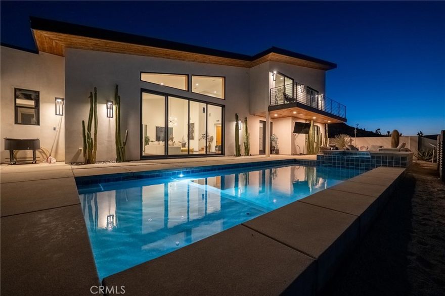 Here's a stunning desert estate, thoughtfully designed to blend modern architecture with the rugged beauty of its natural desert surroundings. Inside, an open-concept floor plan is awash in natural light, featuring clean lines and upscale finishes throughout. The sleek modern kitchen is outfitted with stone countertops, custom cabinetry, an integrated refrigerator, and top-tier appliances.



The kitchen, dining, and living areas seamlessly flow together, all oriented toward panoramic sliding doors that frame expansive desert views to the north. Throughout the main level natural wood accents, black steel fixtures, and polished concrete floors establish a theme of refined, uncomplicated elegance, while each bathroom introduces a touch of contrast with copper fixtures, stylish deco and Marin tile backsplashes.



Upstairs, a balcony overlooks the main living space and leads to the spacious primary bedroom, complete with a private bathroom, walk-in closet, and its own outdoor balcony to further soak in the surrounding desert vistas.



Step outside and you'll find a sparkling pool and spa just beyond the main living area—perfect for indoor-outdoor entertaining. The outdoor space also includes a BBQ area and a built-in fire pit, ideal for relaxing under star-studded desert night skies.



Tech-savvy folks will appreciate this Smart Home is equipped with whole-home audio, high-speed internet, and a security camera system. Ideally located just minutes from eclectic local shops, dining, Joshua Tree National Park, and Pioneertown. This home is a must-see to truly appreciate!