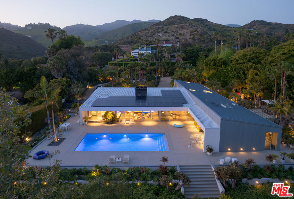 A refined modernist masterpiece, the Shed House has earned well-deserved recognition for its sleek mid-century Palm Springs aesthetic and its exceptional use of absolutely contemporary materials and design. Named for its gently-sloping roof line, the T-shaped residence sits gracefully on a gated parcel of over 1.2 acres at the end of a cul-de-sac on a private road, where it commands sweeping views of the ocean, Point Dume, and Paradise Cove. Custom designed by Michael Boyd and Laurel Broughton, the home was envisioned as a setting for art and sculpture, indoor-outdoor entertaining, and a lifestyle of tranquil comfort. The open layout provides an east-west entertainment axis with expansive, vaulted spaces and walls of glass opening to the pool deck for convivial gatherings, while assuring privacy to bedrooms located in separate wings. At the front of the house is a large circular drive, and an approach with beautiful tropical landscaping that features a quiet covered patio. The main living area is a gorgeous pool and ocean-view living-family-dining great room with high, custom-finished, parchment-glazed maple ceilings, wraparound walls of glass, and custom engineered and stained French oak wide-plank floorboards over a layer of cork for added quiet and comfort. A free-standing double-sided fireplace clad in shimmering, hand-made Heath Ceramic tiles faces the living room and the covered patio at the front of the house. Beneath a large skylight, the top-quality Miele custom kitchen expands from the spacious dining area, with a huge Carrara marble-topped island, generous counter space and custom cabinets, and a large storage pantry. In its own wing, the primary suite, complete with a walk-in closet, has soaring silver-gray stained maple ceilings and a wall of glass opening directly to the pool deck and patio. The dual-sided primary bath also has sliding glass doors to the backyard. On the opposite side of the home's entrance, another hallway leads to two serene en-suite bedrooms, one opening to the backyard, the other opening to a private terrace on the side of the house. The compound has two separate guest accommodations. A detached guest house, which could easily serve as a studio, gym, office, or theater, has a kitchenette and en-suite bath. A second guest house is attached to the garage, where it has a kitchenette and two bedrooms with separate entrances and a locking door between. The two-car garage, with a custom-built disappearing garage door, has laundry facilities, room for a golf cart, and abundant storage space.The ocean-view backyard features a pool with an artful water feature and expansive entertaining deck, a putting green, bocce court, a large dining and barbecue area, a nursery, and meandering pathway to scenic lounging areas surrounded by picturesque lighted and irrigated landscaping. Additional features include a wine cellar, two Tesla Power Walls, commercial grade anodized aluminum glass doors, security system, solar power, a Japanese cedar hot tub, Heath Ceramics in all baths, hidden floor-to-ceiling roller blinds, museum reveal floor trim, and deeded access to the beach and golf cart parking at Escondido Beach. A remarkable achievement in elegant simplicity and livable beauty.