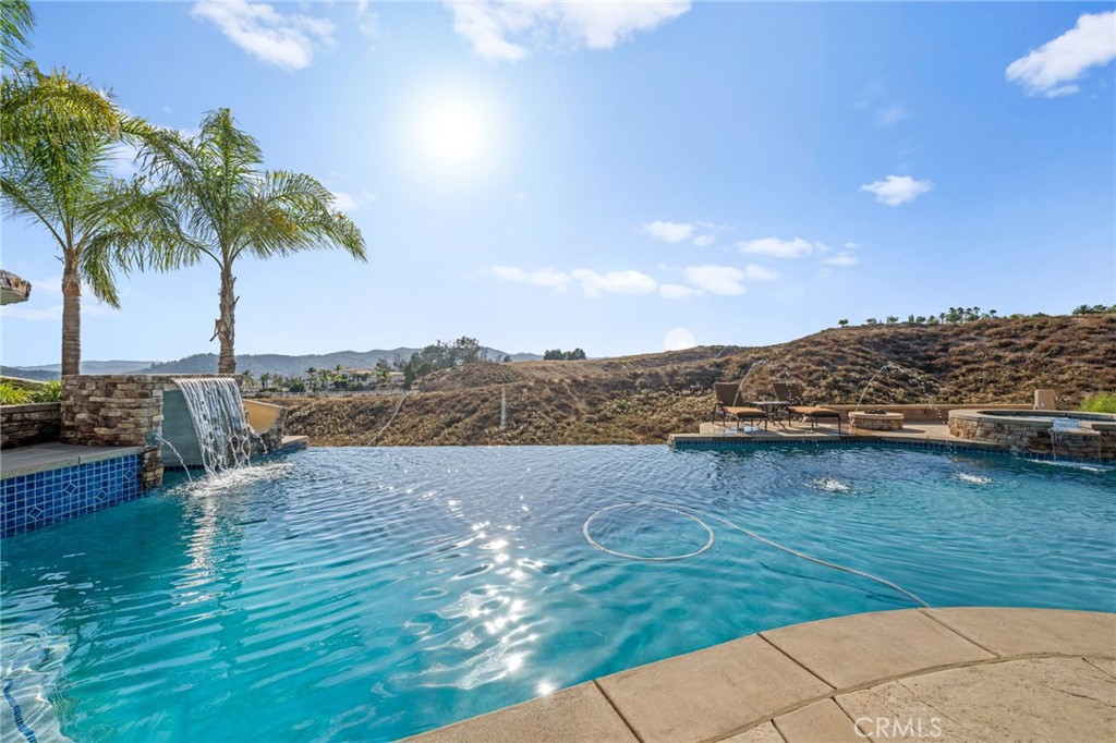 Welcome to Santiago Estates! One of the most prestigious communities in Temecula Valley. This extraordinary estate offers luxury, privacy, and panoramic views all on 3.8 acres. Enjoy 4,661 sq ft in your main residence plus a 1,000 sq ft in the detached guest/pool house built in 2008, perfect for multigenerational living, entertaining, or a private retreat. Step inside through elegant double glass doors into a grand foyer with soaring ceilings, a striking black iron staircase, crown molding, and abundant natural light. The main floor boasts a formal living room, a spacious family room with fireplace, and a chef’s kitchen with granite counters, stainless steel high end appliances, double ovens, and an island with a gas cooktop and sink. The kitchen area also opens to a spacious outdoor patio, ideal for enjoying serene sunrises and sunsets. The main-level primary suite features a fireplace, tray ceilings, a luxurious ensuite bath with soaking tub, walk-in shower, dual vanities, and generous closet space. A private main level guest bedroom with ensuite bath and outdoor access to the veranda offers a great in-law option. Upstairs includes a private office with French doors and open views of the living space below, plus three additional bedrooms and two full bathrooms. Your resort-style backyard includes an infinity-edge saltwater pool and spa, a private illuminated tennis court (north/south oriented), chiminea, covered patio, and pergola with decorative balustrade, all overlooking lush meadows and mountain views. The detached guest/pool house features a full kitchen, bath, and a large upstairs game/theater room. A private drive path leads to the lower two acres, ideal for horses, agriculture, or future expansion. Additional highlights include a ground-mounted fully paid 7.3 kW solar system, tankless water heaters in both homes, HD security camera system, and alarm. Located just minutes from Shopping, Restaurants, Old Town Temecula, Pechanga Casino, distinguished Schools, and award winning Wineries! This one-of-a-kind estate offers the ultimate in California luxury living! Don't miss out, schedule your private showing today!