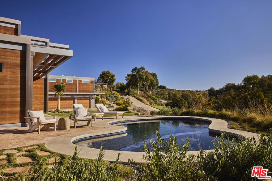 Situated in the heart of Malibu's tranquil Bonsall Canyon, this architectural equestrian estate by Ray Kappe, presents a harmonious fusion of contemporary design and natural elegance. Framed by lush landscaping and open skies, the property exudes refined sophistication while embracing its serene surroundings. The residence itself is a testament to modern minimalism, with clean lines and an open layout that integrates indoor and outdoor spaces seamlessly. Expansive glass walls flood the interiors with natural light and offer sweeping views of the surrounding greenery and ocean. The main living area is anchored by a spacious great room, ideal for both intimate gatherings and larger-scale entertaining. Adjacent, a gourmet kitchen features premium appliances, custom cabinetry, and a dining area designed for leisurely meals that overlook the picturesque grounds. The primary suite, a mix of rustic and modern, has a private deck looking on to nearby vistas, and features spa-like ammenities from the natural landscape settings to high end bathroom finishes that provide extreme comfort.Perched above the garage and thoughtfully detached from the main residence, the private guest house offers a secluded retreat with idyllic views of the ocean and surrounding mountains. Designed with sophistication and comfort in mind, this guest house features an upgraded full kitchen, equipped with sleek, custom-built cabinetry and top-of-the-line appliances that cater to both casual and gourmet cooking. Two guest bedrooms, each with mountain views, provide a serene, resort-like atmosphere. With ample natural light and refined finishes, this guest residence epitomizes luxury and privacy, offering an elevated experience for visitors.Outside, meticulously landscaped grounds provide a sanctuary with a sparkling pool, lounge area, and verdant lawns. Thoughtful pathways meander through the property, leading to equestrian facilities that offer both functionality and aesthetic appeal, all while enjoying a panoramic ocean view. The entire estate is designed to provide an unmatched lifestyle experience, combining privacy, luxury, and the timeless allure of Malibu's coastal ambiance.