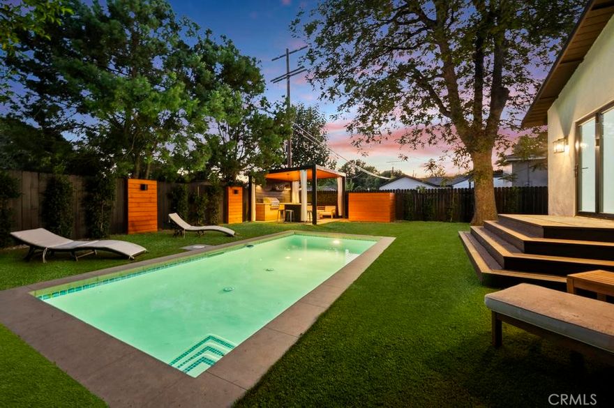 Tucked away on a lush, tree-filled lot, this modern retreat offers the perfect balance of privacy and resort-style living. A remote-controlled iron gate opens to reveal a beautifully reimagined 5-bedroom, 4-bathroom home showcasing timeless design and high-end upgrades throughout. Inside, the open-concept floor plan is anchored by White Oak hardwood floors and a sleek designer kitchen with quartz countertops, under-lit cabinetry, matching Thor appliances, and a built-in three-temperature wine refrigerator. The expansive primary suite overlooks the serene backyard and features a spacious walk-in closet along with a spa-inspired ensuite highlighted by dual sinks and a curb-less, zero-entry shower. Three additional designer bathrooms echo the same attention to detail with walk-in showers and luxury finishes. Step outside to your private paradise: a brand-new sparkling pool shaded by mature trees and complemented by a resort-style cabana. Designed for entertaining, the cabana is complete with an outdoor kitchen, built-in Spires BBQ, dual-temperature wine fridge, mounted TV, overhead lighting, and a cozy fire pit. Recent upgrades provide peace of mind, including a new roof, HVAC system, water heater, all-new copper and PEX plumbing, smooth stucco exterior, stamped concrete driveway, and low-maintenance synthetic turf in both the front and back yards. A rare blend of sophistication, comfort, and modern California living, this home is a true retreat designed for both relaxation and entertaining.