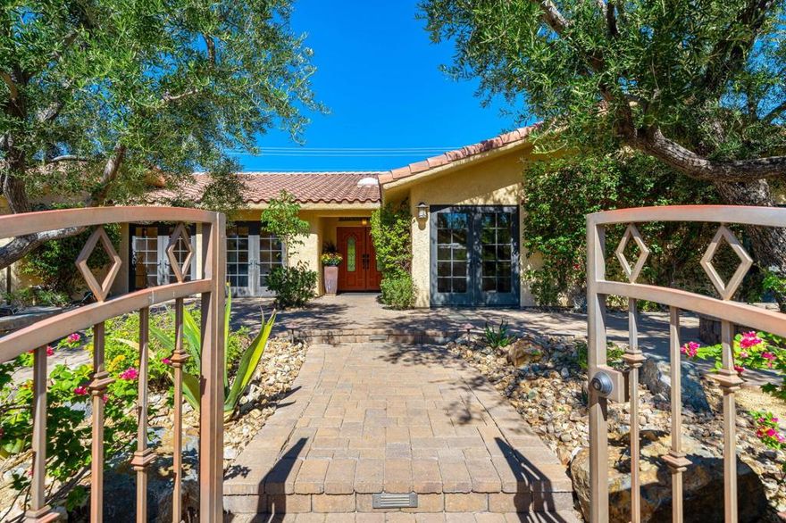 Experience desert sophistication in this inspired 2,720 sq. ft. home featuring a spacious backyard with pool, spa, and stunning mountain views. Situated on a generous 0.27-acre lot, this residence showcases a beautiful enclosed front courtyard with lush desert landscaping and breathtaking southwest mountain views, welcoming you into your own private oasis. Step through the double front doors into the expansive living room, where vaulted ceilings and a central fireplace anchor the space. A wall of sliding glass doors seamlessly connects indoor and outdoor living, drawing you toward the dining area and chef's kitchen. Ideal for entertaining, the kitchen features rich wood cabinetry, premium appliances, soaring ceilings, and a large island with additional bar seating. The adjacent dining area includes a stylish wet bar and wine fridge; perfect for gatherings. Just off the kitchen is a family room with french doors that open out to a private courtyard. This versatile multi purpose room offers ideal flexibility for an office, den, or media room. The expansive backyard and outdoor kitchen are true highlights of this home, showcasing a saltwater pool and spa, a wide-open lawn, and stunning west-facing mountain views. The built-in outdoor kitchen, set beneath a covered pergola, includes a BBQ, wine refrigerator, and convenient French doors connecting directly to the main kitchen. On the east end of the home, a hallway leads you to 3 bedrooms and 4 baths, ensuring a thoughtful separation between living and rest spaces. The primary suite offers an elegant retreat with a stone fireplace, a luxurious ensuite bath featuring a soaking tub and separate shower, and a spacious walk-in closet with custom built-ins. Sliding doors open to the backyard, blending indoor comfort with the tranquility of private desert escape. The two additional guest bedrooms each feature their own ensuite bath and spacious walk-in closet, providing comfort and privacy. Guests will love the French doors opening to the front courtyard. The home additionally includes a spacious three car garage. Originally showcased as the neighborhood's model home, this residence offers a rare opportunity to personalize and make it your own-now at a new, more accessible price point. Just minutes from downtown Palm Springs, it's ideal as a lavish desert retreat or a comfortable family home. Experience the perfect blend of style, comfort, and desert sophistication. Your Movie Colony Palm Springs dream home awaits!
