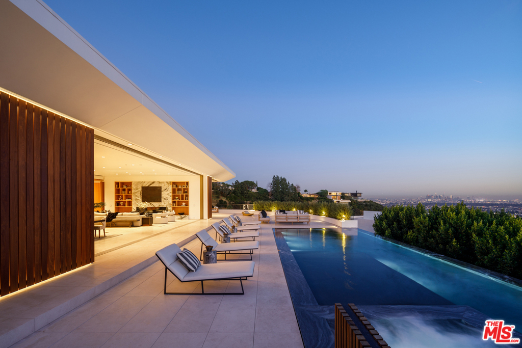 Private, amenity-rich entertainer's paradise on a quiet cul-de-sac in the Hills, moments to Sunset Strip. Boasting a sun-filled open floor plan, custom finishes & breathtaking city vistas, this contemporary oasis is ideal for unwinding in the luxurious comforts of home. Bright, airy floor plan & wall of glass pocket doors create a space for indoor-outdoor living. High-end appliances, built-in espresso machine, wine fridge, ample cabinetry & luminous marble backsplash, chef's kitchen opens to formal dining & living w/marble fireplace & staggered shelves. Expansive, opulent owner's suite w/spa tub, grand shower, dual sink vanity, large walk-in closet & full-height disappearing glass walls providing views and direct outdoor access. Amenities include 2nd lower-level primary suite w/steam shower, movie theater, office w/full bath, bar, wellness space, car gallery w/auto turntable, wine cellar, infinity pool/spa, endless outdoor living spaces & so much more. The owner's suite & great room open to a wraparound terrace w/adjacent fire-pit deck for staying cozy on even the coolest evenings, and access down to the patio for open-air dining or taking a dip in the pool & spa. Off to the side, a delicately hidden outdoor kitchen leads to the gated motor court. When the city lights beckon you away from your hillside oasis, Sunset & best of LA are just moments away.