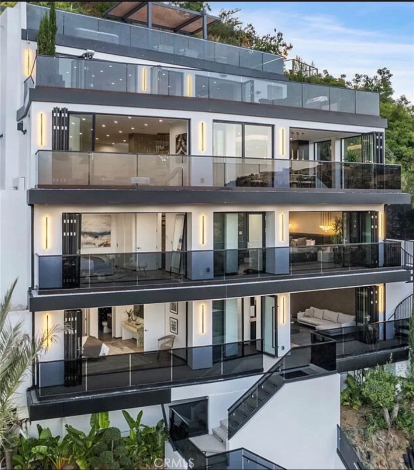 Perched in the Hollywood Hills with jaw-dropping downtown and canyon views, this newly built 4-bedroom, 6-bathroom residence is a showpiece of contemporary design and luxurious living. Two expansive rooftop decks include a spa-style hot tub, sauna, fire pit lounge, built-in BBQ, dry bar, and a striking two-tier waterfall that flows into the heated pool and spa. Perfect for entertaining or relaxing in total privacy. Inside, the open-concept living space features a chef’s kitchen with Thermador appliances, hidden double refrigerators, and a waterfall quartz island, flowing into the dining area and living room with terrace access. The spacious primary suite boasts a fireplace, custom walk-in closet, and spa-like bath with soaking tub and double rainfall showers. Each guest bedroom includes ensuite baths and walk-in closets. A private lower-level guest suite offers its own entrance, kitchen, laundry, and outdoor space — ideal for extended stays or staff quarters. Additional features include a 2-car garage with EV charging, glass elevator, multi-zone HVAC, and solar-ready infrastructure. Surrounded by mature olive and bonsai trees, this home blends tranquility with dramatic design — a true Hollywood Hills gem.