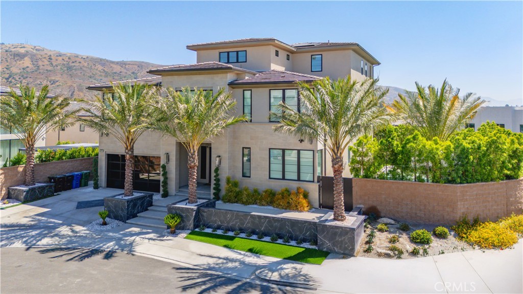 Introducing a rare opportunity to own the stunning Santi Elite Summit Model, one of the largest and most distinguished floor plans in the prestigious Westcliffe community. Perfectly positioned on a sweeping 13,000+ sqft corner lot at the end of a quiet cul-de-sac, this architectural showpiece offers captivating panoramic views of the mountains, twinkling city lights, and rolling hillsides. Designed for resort-style living, the private backyard is a true sanctuary. A state-of-the-art saltwater smart pool with beach entry, tranquil water features, and a dramatic water wall sets the tone for outdoor elegance. The detached spa lounge area features a freestanding TV wall, an expansive fireplace flanked by custom fire pilasters, and multiple fire features an entertainer’s dream with a view. Over 100 mature trees surround the property, creating a sense of privacy and natural serenity rarely found. Recently, the entire exterior was fitted with discreet bird netting an effective and humane solution to prevent birds from entering unwanted areas, adding another layer of thoughtful care and value to the home. Inside, the home is a masterpiece of modern design, showcasing refined finishes, thoughtful upgrades, and curated details throughout. The open-concept layout is complemented by a sleek built-in wet bar and an impressive three-story floating staircase that leads to a versatile upper-level bonus room with its own full bath and expansive view terrace. Window coverings throughout include a combination of custom shutters and electric shades, blending style with convenience. Wellness and sustainability are seamlessly integrated with a private home gym, whole-home water softener and purification system, smart irrigation, and fully paid solar panels. Tech-forward conveniences include EV charging stations—two inside the garage and one exterior—and premium sliding glass doors that create a seamless indoor-outdoor living experience. Enhanced with builder upgrades and custom options, this residence stands as a symbol of sophistication and distinction. Located within the highly desirable Porter Ranch community, enjoy close proximity to top-rated public and private schools, including the renowned Porter Ranch Community School and Sierra Canyon.
