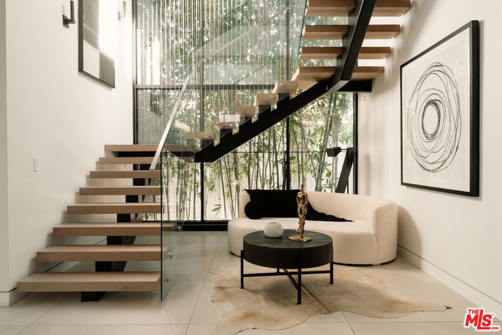Welcome to Zen: A serene statement of modern luxury where elevated design and mindful living intersect in the heart of Melrose. Set behind gates in the vibrant heart of the Melrose District, this striking architectural residence presents a private sanctuary of modern sophistication designed to elevate everyday living with resort-style amenities, serene interiors, and cutting-edge innovation. A dramatic entry opens to soaring ceilings, expansive walls of glass, and gallery-like proportions bathed in natural light. Clean lines and natural textures evoke a sense of calm throughout, while thoughtful design details including a dramatic floating staircase, architectural lighting, and organic materials set the tone for elevated, yet approachable luxury and contemporary elegance. Zen features 5-bedrooms and 6-bathrooms spanning across 5,300 sq. ft. of meticulously designed living space and offering an unmatched combination of high design, functionality, and tranquility in a modern contemporary style. An entertainer's dream, the expansive open-concept living and dining areas are anchored by a dramatic fireplace and flow effortlessly into a gourmet chef's kitchen outfitted with top of the line Wolf appliances, custom cabinetry, a spacious center island, and sleek stone countertops. Retractable glass doors disappear to reveal a seamless indoor-outdoor experience, leading to your private backyard oasis. With wellness and lifestyle at the forefront, Zen comes with a private gym, perfect for morning workouts or mindful movement and a set of resort-level amenities including a sparkling pool and spa for sun-soaked afternoons, a cold plunge and sauna for restoration and renewal, and multiple lounge areas surrounded by lush, thoughtfully landscaped greenery providing your own modern retreat in the middle of the city. The primary suite is a masterclass in luxury and serenity, featuring a spacious layout, private balcony, spa-like bath, a free standing soaking tub and walk-in rain shower, and a spacious boutique-style closet. Each of the additional en-suite bedrooms offers ample space, designer finishes, and the same sense of understated luxury as seen throughout the property. At the crown of the estate is an expansive rooftop deck featuring panoramic, unobstructed 360 degree views that stretch from Downtown Los Angeles to the iconic Hollywood Hills and includes a built in rooftop grill and bar and a fire pit presenting an extraordinary setting for sunset cocktails or starlit dinners. For those who appreciate intelligent living, the home is fully integrated with a state-of-the-art Control4 smart home system, allowing you to manage lighting, climate, sound, and security with ease from anywhere. Enjoy rich audio throughout with built-in speakers in every major room, perfect for ambient music, entertaining, or immersive media experiences. The property is also equipped with a comprehensive security system, including strategically placed cameras and remote access, offering both peace of mind and privacy. Located in the vibrant Melrose District, you're just moments from some of Los Angeles' most acclaimed shopping, dining, and entertainment yet the home's privacy and peaceful atmosphere make it feel like a world of its own. This is not just a residence, it's a lifestyle. Luxurious, soulful, and effortlessly cool, Zen is the type of residence that redefines what it means to live well in Los Angeles.