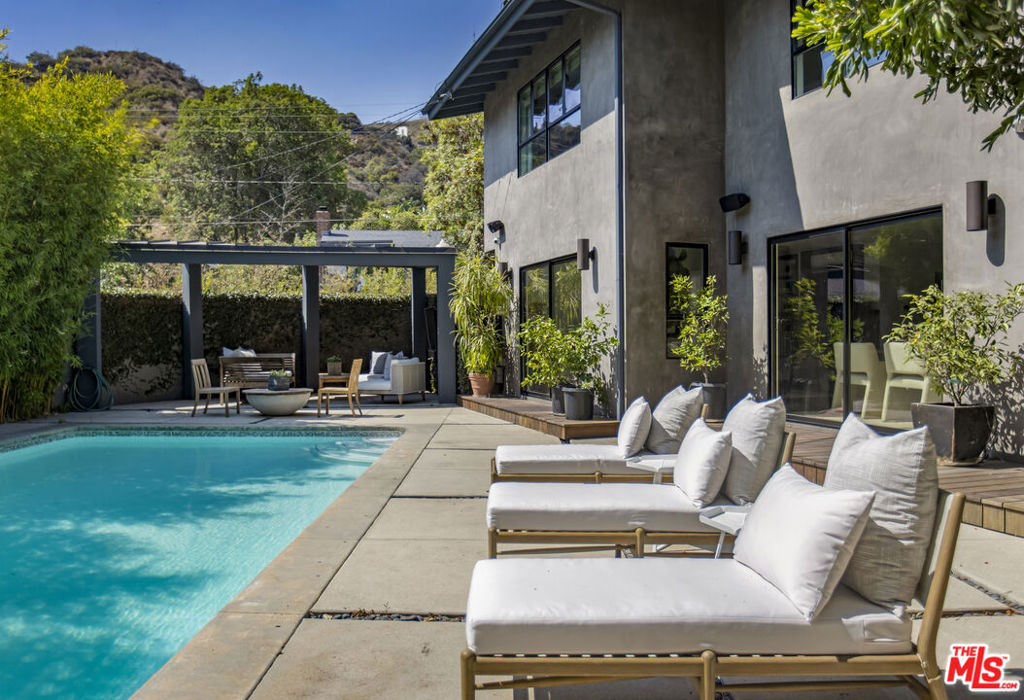 Located at the very top of Legendary Beachwood Drive, this stylish Mid-Century residence is the epitome of indoor-outdoor California living with open plan living space leading to multiple flat private outdoor areas with pool, patios and gardens. Behind walls and mature landscape a stone path leads to the covered front entrance. Formal entryway leads to expansive living area with fireplace and separate dining area; with multiple sliding doors opening to the outside. Flowing directly into the main rooms, the seamless cooks kitchen is upgraded with chic wooden cabinets, stainless appliances and unique window-backsplash spilling sunlight onto the counter tops. The upstairs level is luxurious with three spacious full en-suite bedrooms with tiled baths; featuring a double-room primary suite with office or nursery flex-space and a view into the canyon. The flat yard exudes privacy and natural beauty, encircled with bamboo and hedging, with a large stunning swimmers pool as focal point. Private covered and open patios encircle the yard and pool, with a separate section for gardening and another area with flat grassy yard. Parking is a breeze with driveway and attached direct access garage. Welcome to your prime spot on the street: Take a stroll to the village for lunch or groceries, or explore 4200 acres of the unspoiled natural trails in Griffith Park on horseback at the nearby Sunset ranch. Life is good under the Hollywood sign!