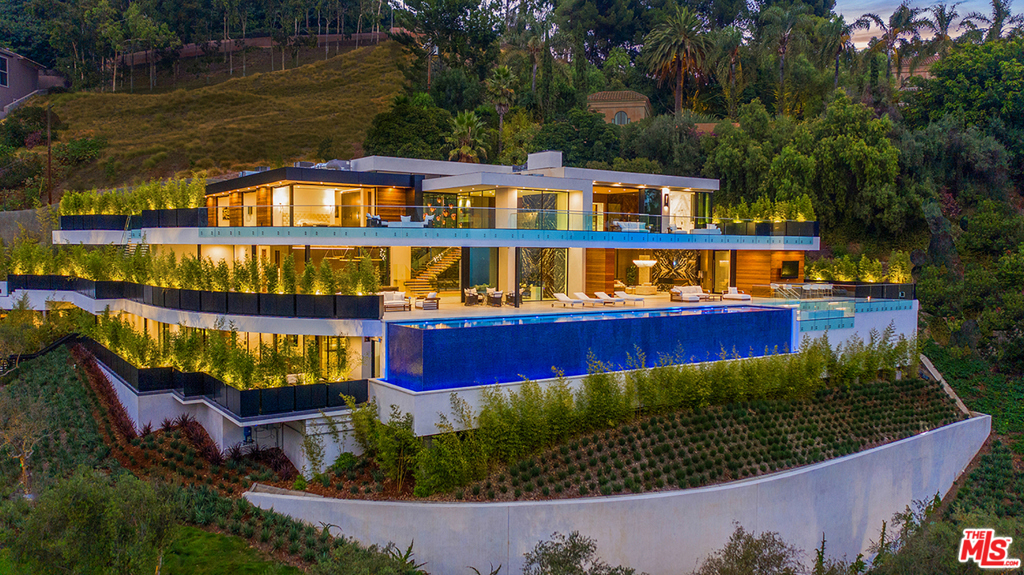 In a quiet neighborhood minutes from the heart of Beverly Hills sits 1300 Beverly Estate Dr., a 3-story retreat that captures panoramic views of the city below and ocean beyond. Designed by Lorenzo Cascino of design firm Visionnaire, this 12,500-square-foot home is filled with distinctive amenities and bespoke decorative elements. Enter the lower level from the terrace, which runs the length of the homes view-facing facade. This floor encompasses a game room, fitness studio, a 600-bottle wine wall and theater. The homes main level features a showroom garage, chefs kitchen and living areas. On the third level are 3 ensuite bedrooms and master suite. Additional features include an 80-foot-long infinity pool, motor court and smart home technology system. Located minutes from the entertainment of West Hollywood, 1300 Beverly Estate Dr. is an architectural marvel ideal for entertaining and sophisticated everyday living.