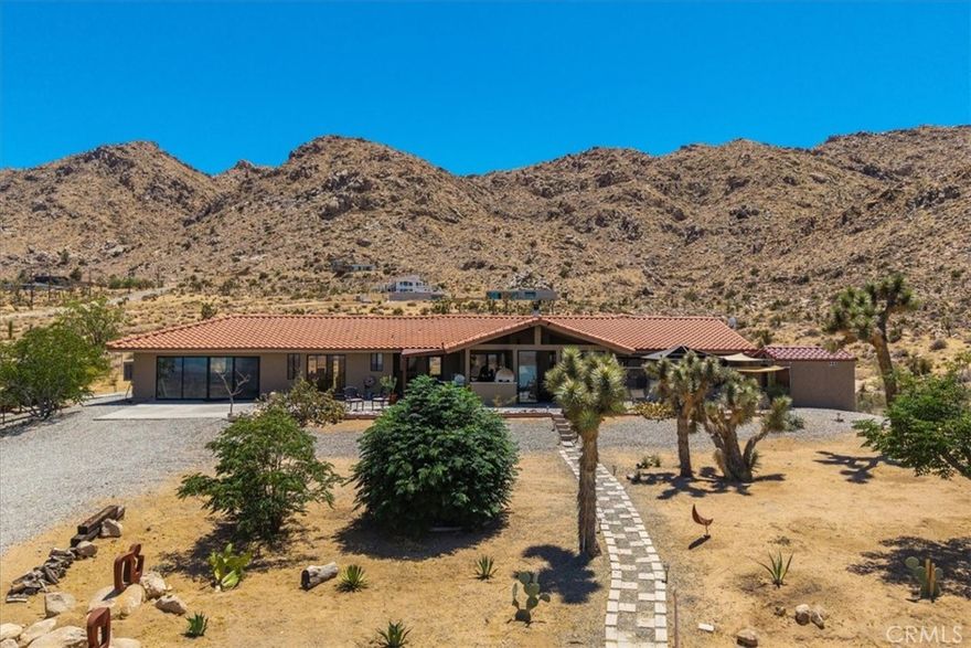 7880 Wesley Road, in the Friendly Hills neighborhood of Joshua Tree, is a thoughtfully designed desert retreat set on 2.7 acres with panoramic 180-degree views of the Morongo Basin and beyond. The main house offers approximately 2,300 square feet of living space (not including the artist studio) and features four bedrooms, including a spacious primary suite created by combining two bedrooms, a large office created from a fourth bedroom, and a guest bedroom with an ensuite bathroom that includes an oversized shower. The home has three bathrooms in total, including a full bath with a soaking tub adjoining the primary bedroom, a second ensuite bath, and a third with a pedestal sink near the office.



Inside, the home is finished with porcelain tile flooring throughout and features extra-wide hallways and large closets in the bedrooms and hallways for plenty of storage. The living room includes a wood-burning fireplace and a custom-built wall unit with a large TV and network cabling. The open kitchen features granite counters, recessed lighting, and a large pantry. There is also a separate laundry room with generous storage space and a washer and dryer included.



Outdoor living is exceptional, with a full outdoor kitchen that includes granite counters, a built-in BBQ, smoker, sink, and wood-burning pizza oven, all adjoining a partially enclosed outdoor dining area. The property also features a cedar-planked sauna with a dressing room, an outdoor shower, and a spa. A fully refurbished 30-foot Silver Streak trailer serves as a charming guest house, complete with a covered redwood deck offering a canyon view.



Creative and hobby spaces abound, including a artist studio with evaporative cooling and sliding glass doors to the north, and an 1,800 square foot climate-controlled steel shop that doubles as a man cave and gym. A climate-controlled greenhouse adjoins the shop, adding to the property's versatility.



The home features dual-zone comfort conditioning as well as evaporative cooling, powered in part by an 11kW owned solar system. Approximately two acres of the property are fully fenced, making it ideal for privacy, pets, or gardening. This property offers a rare blend of peaceful desert living, artistic inspiration, and practical amenities just minutes from the heart of Joshua Tree and the national park entrance.
