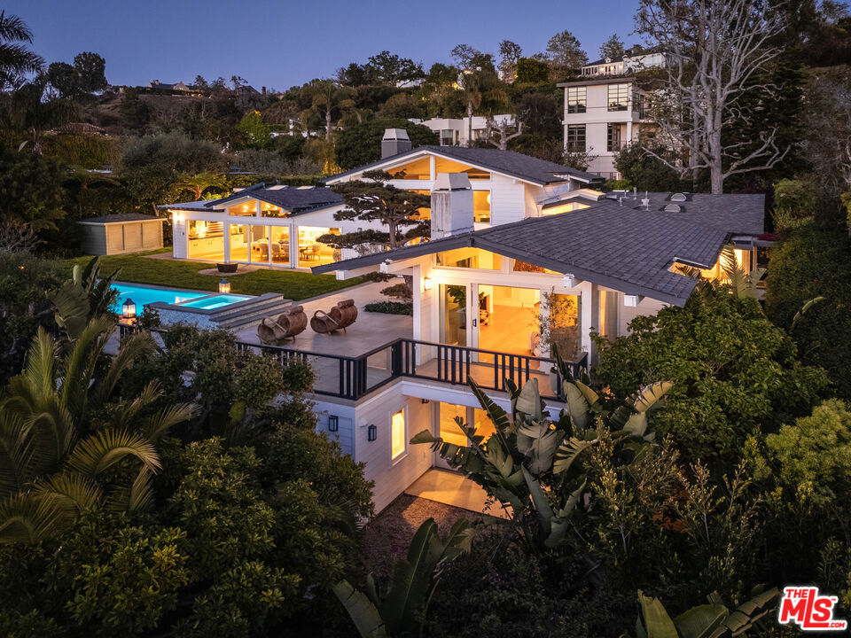 1135 Ravoli Drive, located in the Riviera of Pacific Palisades, blends thoughtful design, complete privacy, and indoor-outdoor living crafted for the most discerning eye. The moment you arrive, the exquisite front garden accentuated by blooming wisteria represents the tranquil sophistication of the entire property: effortless, yet completely captivating. Inside, 16-foot ceilings surrounded by glass windows and doors allow rich natural light to pour in. The interiors unfold poetically with an open-concept indoor-outdoor living space, flowing through curated textures and design at every turn. The living room flows seamlessly into the dining area, kitchen and lounge, offering a space equally suited for everyday living as it is to elegant entertaining. The private tiered backyard is a retreat, with a sparkling pool and spa and 70 year old Sensei tree sculpted by a master Sensei gardener, enhancing the peacefulness of this serene retreat. Lush and varied tropical landscaping brings depth and texture to the yard, while its western orientation provides breathtaking sunset views each night. A grassy lawn flows through the lower tier, encompassing raised vegetable beds and mature fruit trees including: peach, fig, lemon, lime, apple, tangerine, yuzu, guava and avocado, leading to a large chicken coop. The richly sunlit primary suite is a spacious sanctuary of peace and calm, surrounded by nature and designed for relaxation. With walls of glass windows and doors, the primary is complete with a fireplace, sitting area and western sunset-view balcony. The spacious walk-in closet and en-suite bath are serene, light and airy. A second primary guest suite or media room with a separate entrance provides a dramatic yet cozy retreat, complete with a beautiful Japanese designed en-suite bath, fireplace, walk-in closet, and custom Japanese soaking tub with a lush backdrop of tropical greenery. Two additional garden-opening bedrooms occupy their own separate wing with a refined, exotic modern bath accented with organic design details. Each opens to its own lush private garden patio. In a separate wing, you'll find a powder room, laundry room, two-car garage and a fifth bedroom or office with its own en-suite bathroom. 1135 Ravoli Drive is more than a home, it's a personal resort. Every detail has been carefully considered, yet the experience remains effortless. It is impossible to articulate without stepping inside. Once you're there, you'll never want to leave.