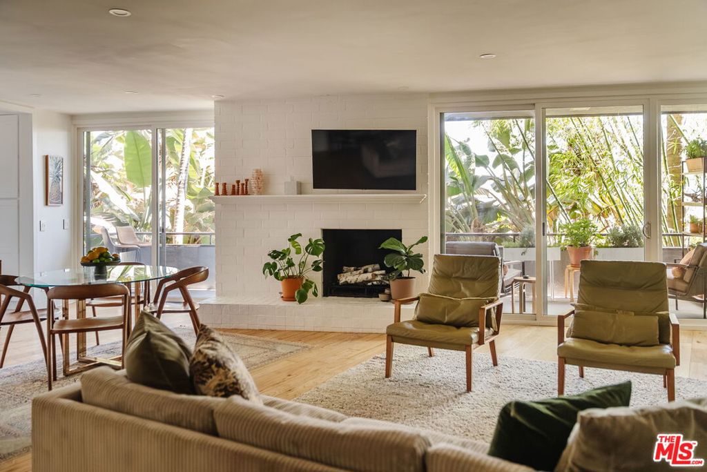 Wrapped in light and style, this corner residence pairs timeless character with thoughtful updates. Located in a boutique building with only four homes per floor, the south- and east-facing unit enjoys leafy views, incredible natural light, and just one shared wall for added privacy. A double-door entry leads into an airy, open layout where living, dining, and kitchen spaces connect effortlessly ideal for both entertaining and everyday living. The generous living room features a brick fireplace and sliding doors that open to a large, lushly surrounded balcony. The adjacent dining area and wet bar create the perfect setting for gatherings, with quartz counters and a dramatic marble herringbone backsplash adding a refined touch. The kitchen has been beautifully remodeled with waterfall-edge quartz counters, matching full-height backsplash, and reverse osmosis water filtration. Offering two bedrooms and two baths, the home's private wing includes a spacious primary suite with a walk-in closet, motorized blinds, and a serene en suite bath. The guest bedroom is equally inviting with a large cedar-lined closet and custom wall detailing, and is served by a modern guest bath with a walk-in shower. Throughout the home, red oak hardwood floors and designer finishes create a warm, stylish atmosphere. Additional highlights include central HVAC, abundant storage, in-unit washer/ dryer and an unbeatable location just moments from the Sunset Strip, Equinox, Gelson's, and some of LA's best dining, coffee, and nightlife. A turnkey home in a coveted West Hollywood pocket, ready to enjoy from day one.