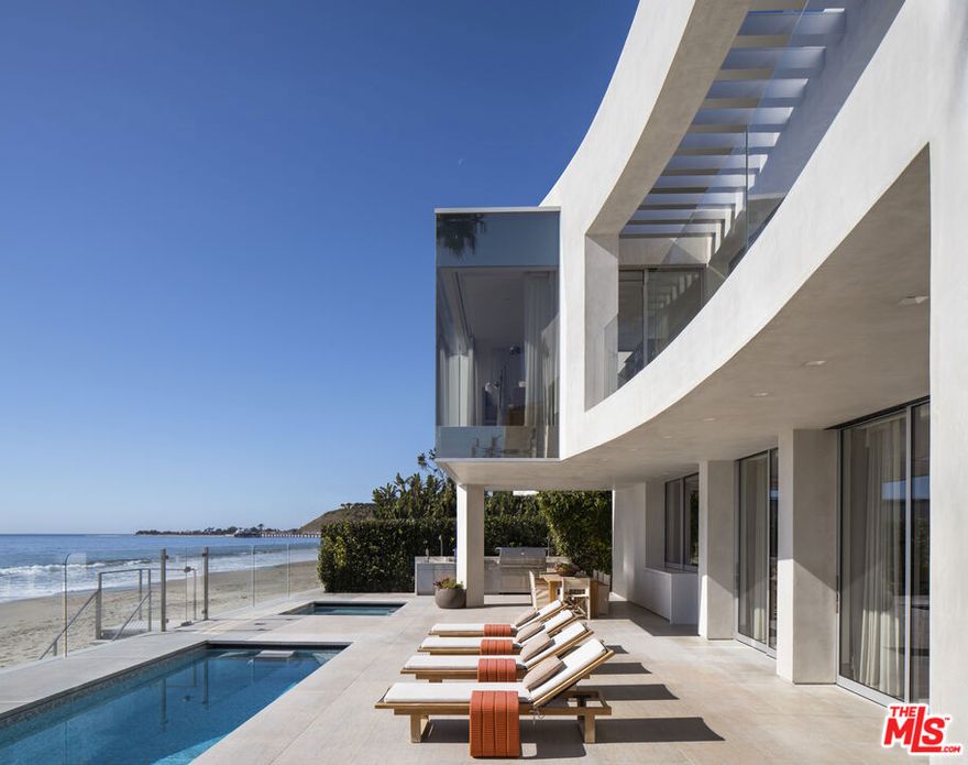 With impeccable architectural credentials and one of Southern California's most enviable settings, this remarkable beachfront estate is spectacular and livable in equal measures. Majestic lines, luxurious appointments, and incomparable views are perfectly scaled to priceless Carbon Beach, where the property occupies some 70 feet of shoreline frontage. The award-winning Landry Design Group transformed the solid Modernist bones of the Buff and Hensman original to a dramatic residence with substance and style suited to the 21st century. Gated and exceedingly private, the home's walls of glass and generous patios, courtyards, and decks provide seamless flow for lavish entertaining and sparkling vistas of shoreline, ocean, islands, and sky. On the lower level, the main living areas are spacious and open, with soaring gallery walls, floor-to-ceiling glass, and exquisite detailing in wood, metal, and stone. Just outside is a gorgeous beachfront patio complete with a covered dining area, outdoor kitchen and barbecue, pool, Jacuzzi, a large outdoor living room, and private steps to the sand. A pass-through window opens to the ocean-view kitchen, which is equipped for the professional chef with top-grade appliances, island with bar seating, and a walk-in pantry. Completing the lower level is a large home theater that opens to the front courtyard. On the upper floor, the all-en-suite bedrooms include a serene primary suite with stunning views, a sitting area/office, a view balcony, walk-in closet, and luxurious bath. There is also an en-suite gym/bedroom on this level, which has a service counter, beverage cooler, and dumbwaiter lift. Topping this magnificent residence is an enormous roof deck that is accessed through dramatic retractable glass roof. For entertaining, lounging, or star-gazing, this resplendent space is equipped with a wet bar with seating, barbecue, fire pit, dining area, Jacuzzi, and exquisite views. The residence has many additional smart-home features, including an automotive turntable in the driveway. With an exterior distinguished by soaring walls of sweeping bird-wing curves and an interior of harmonious beauty, this inspired Carbon Beach estate has graced magazine covers and won awards for its thoughtful renovation. It is a legacy of contemporary design.