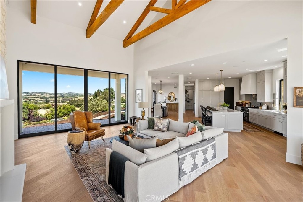 This exquisite blend of modern luxury and timeless elegance is located in the prestigious guard-gated community of Santa Ysabel Ranch. Newly constructed and designed for those with discerning taste, this home offers 4,426 sq. ft. of refined living space, showcasing breathtaking views from nearly every room. The exterior captivates with its smooth stucco finish, accented by chic grey stone details. Step inside to an expansive open-concept layout, with hardwood floors throughout. The living room, featuring soaring ceilings and a dramatic floor-to-ceiling stone fireplace, flows seamlessly into the dining area and a state-of-the-art chef’s kitchen. The kitchen is a culinary masterpiece, boasting a 10-foot island, quartzite countertops, a coffee bar, and a walk-in wine room, ideal for collectors. The main level includes a luxurious ensuite bedroom, while upstairs, the primary suite serves as a tranquil haven. It features a spa-inspired bathroom, designer walk-in closet, sitting room, and a private balcony with sweeping vineyard views. The upper floor also offers a family room, den/media room, two additional bedrooms, and a powder room. Crafted with meticulous attention to detail by RBU Building & Design, this home epitomizes luxury living, where elegance, comfort, and sophisticated design come together in perfect harmony.