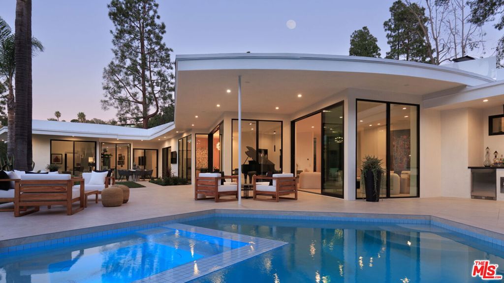 Welcome to this stunning 5 bedroom/6 bath Mid-Century home in Beverly Hills' coveted Trousdale Estates. Situated on nearly half an acre of flat land, you'll discover the quintessential Trousdale layout with walls of glass showcasing the over-sized pool and twinkling canyon lights. Pull behind the gate, and you'll feel worlds away from LA. Enter the foyer, and you'll immediately be drawn into the grand living room with statement fireplace, a sunken bar and an adjacent formal dining room. The doors open to provide seamless access to the expansive outdoor patio with flexible seating areas, an outdoor dining area and firepit. The large, original pool has been newly re-finished and is ready for a leisurely afternoon dip or a quick round of laps. Beyond the pool sits an expansive lawn. Big enough for a game of football or soccer, and serene enough for an afternoon yoga session in the shade of a structural oak tree and mature palms in a park-like setting. Three bedrooms sit at the back of the property. The primary bedroom anchors the home, offering dual closets and an en-suite bathroom with soaking tub. Two additional bedrooms and a large office with patio round out the rear of the home. Afternoon sun pours into the chef's kitchen with island seating and an over-sized breakfast nook. You'll also find an additional bedroom perfect for an au pair or in-law. Beyond the dining nook lies a large family or game room plus an additional bedroom perfect for guests. Complete with a separate entrance this area could also be utilized as a studio space or private home office. Originally built in 1960, this home was fully renovated in meticulous detail over the last year-plus. Its versatile layout offers just the right home for a wide range of buyers.