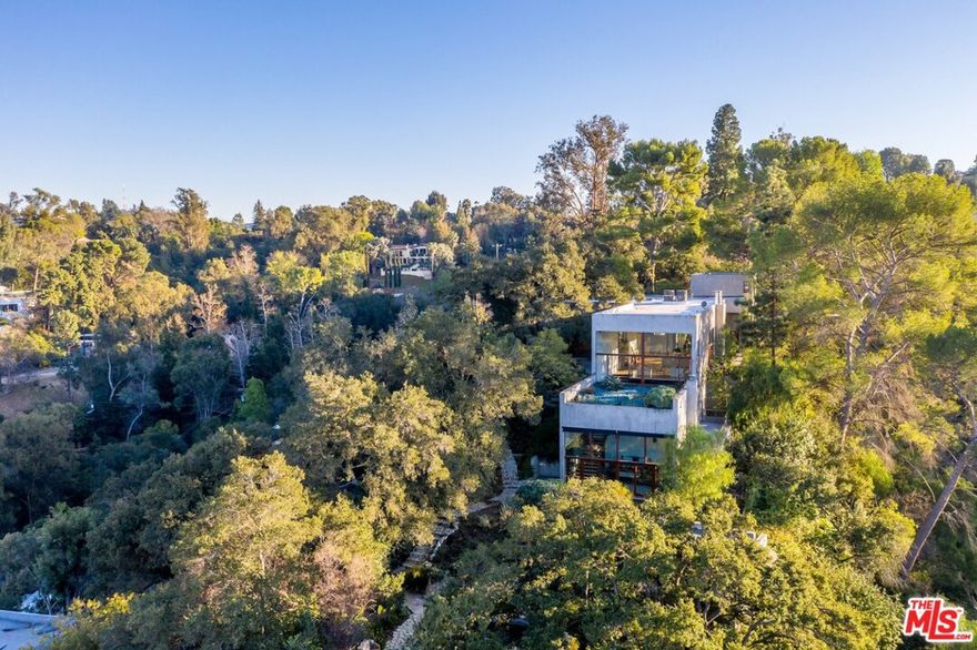 As featured in Architectural Digest, this modern estate sits on approximately 2 acres accessed via a private gated drive and nestled in the most breathtaking setting. Mature trees and an unbuilt canyon surround 3 modern structures overlooking the entire valley. The main home features dramatic 16' ceilings, expansive windows offering beautiful natural light, and views from every room.A separate structure contains a large 3-car garage with private studio/guest suite above, located adjacent to a large motor court. Follow the path down to find carefully placed guest/pool house with its own parking adjacent to a dramatic pool and spa. Sophisticated and restrained design hidden in the most natural and tranquil surroundings inspire a healthy, creative and serene lifestyle.