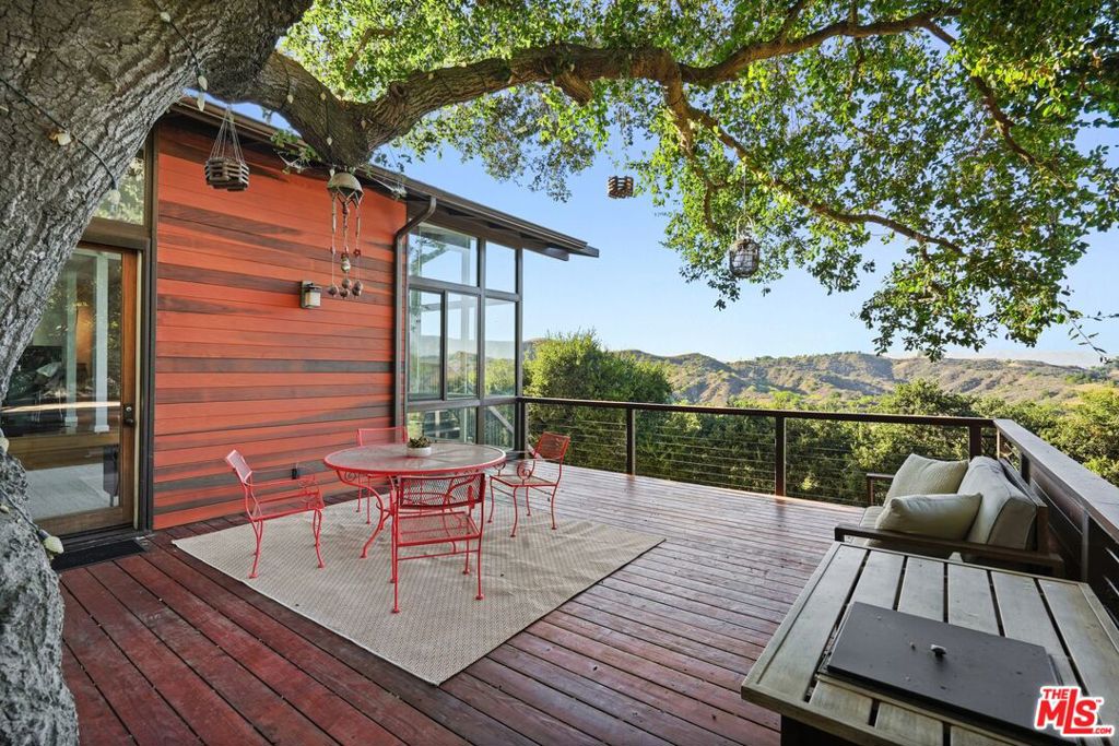 Mid-Century Sanctuary with Guest House, and Studio Apartment. Tucked away in the poetic hills of Topanga, where the scent of sagebrush mingles with coastal air and the canyon light shifts like watercolor, this mid-century retreat rises from the earth like sculpture. Built in the 80s by a Topanga Family of master builders, this home has the soul of a 1960s architectural, with towering walls of glass, but is built with modern building methods and amenities that live more fully in our present. Set across 6 lots totaling more than half an acre of pure California dreaming, this is not merely a home, but a dream made real. Framed in clean, modernist lines and softened by warm woods and welcoming landscaping, the main residence offers three bedrooms and two baths, with interiors that channel the understated elegance of a bygone era. Vaulted ceilings open skyward, while walls of glass dissolve the boundary between indoors and the wild beyond, inviting the Santa Monica Mountains in like an old friend. A sunken living room anchors the space with quiet drama, its hardwood floors catching golden light, while a fireplace hums softly against the cool hush of canyon evenings. The sleekly updated kitchen gleams with high end stainless appliances, huge windows, stone counters, and cabinetry that soars up to the 14 ft ceilings. The primary suite is a private escape, complete with a dreamy, custom, walnut, walk-in closet with a view, private viewing deck, and a spa-like bath where a glass-wrapped shower overlooks the green hills of the nearby state parka tableau, framed in stillness and sky. The living room flows onto a huge deck, set in the wide vistas. Steps lead to paths meandering through native landscaping and terraced gardens that create a sanctuary for the senses. A gorgeous, built in, Charbroil outdoor kitchen nestles under an arbor, perfect for grilling up a celebration! Dine beneath a canopy of oaks, sip wine beneath the stars around the gas fire pit, or soak in the hot tub while hawks wheel overhead. Here, every detail whispers of retreat and ritual. Two thoughtfully appointed guest units, a charming detached cabin at the top of the property, with loft, kitchenette, bath, and deck; and a second large studio apartment, with private entry, kitchen, and bath, offer room for reflection, creation, or connection. Set along a private drive just moments from the vibrancy of the center of Topanga, with its restaurants, galleries, yoga studios, and charming shops, in a quiet neighborhood surrounded by trails, this graceful home is close to Malibu, the Valley, and all that LA has to offer. This is a home for artists, dreamers, and seekers of beauty. A place where architecture meets wilderness in elegant accord, and where every sunrise feels like a new beginning. This is a Topanga Miracle, refined, rare, and waiting for you.