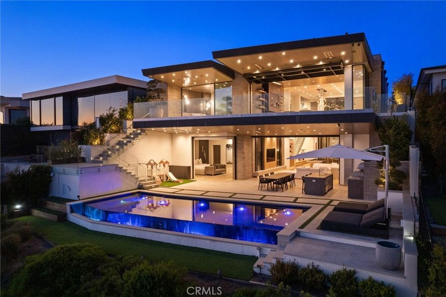 Positioned in the most prestigious front-row enclave of Irvine Terrace, this architectural masterpiece offers an extraordinary opportunity to own one of the most coveted vantage points in all of Newport Beach. Designed by the acclaimed Brandon Architects and encompassing over 7,000 square feet of meticulously curated living space, this residence is a testament to elevated design, bespoke craftsmanship, and uncompromising quality. Framed by unobstructed views of Newport Harbor, Catalina Island, and city lights, the home’s grandeur immediately welcomes you. Soaring 11.5-foot ceilings and wide-plank white oak floors establish a warm, yet sophisticated palette, while custom finishes and architectural details speak to a level of thoughtfulness rarely seen. Crafted for a discerning lifestyle, the floorplan offers 5 expansive bedroom suites, a private office, and 8 artfully designed bathrooms. An integrated Savant smart home system provides seamless control over every element—from lighting and climate to security and entertainment. Every amenity has been conceived with luxury in mind: a private wellness studio and gym, a state-of-the-art screening room, and a 1,300-bottle, climate-controlled wine cellar secured with a biometric security feature. A full entertainer’s bar, elevator, and 4-car garage elevate both convenience and experience. The heart of the home lies in its open concept living and dining spaces, anchored by a chef’s kitchen equipped with Gaggenau appliances, a Quartzite-clad Island, and an adjoining prep kitchen for seamless hosting. Floor-to-ceiling Renlita doors vanish to reveal uninterrupted indoor-outdoor flow, where refined comfort meets dramatic coastal vistas. The primary suite is a private retreat with its own expansive terrace overlooking the harbor, a sleek stone fireplace, and a spa-quality bath complete with soaking tub and steam shower. The walk-in wardrobe—custom-built with suede and leather detailing—is worthy of a private atelier. On the lower level, you will find a secondary primary suite, additional guest quarters, and a grand entertaining lounge open to a resort-style outdoor living space. The infinity-edge pool, built-in BBQ kitchen, and multiple lounge areas offer a front-row seat to Southern California’s most iconic sunsets. This is more than a home—it’s a rare, legacy-caliber estate for the individual who seeks the exceptional.