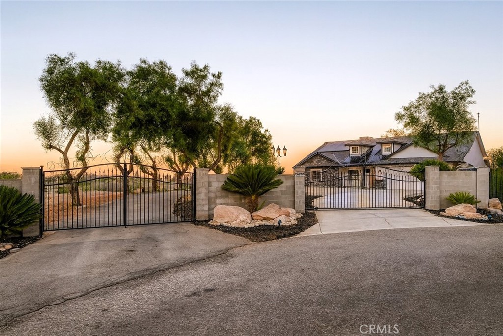 This gated contemporary ranch estate blends timeless charm with modern design, perched on a bluff overlooking a lush citrus orchard and bordered by a peaceful creek. The home’s low-pitched roofline, dormer windows, and expansive single-story layout evoke classic ranch architecture, while custom stonework, stucco finishes, and modern accents create a warm yet sophisticated feel.
Inside, the updated kitchen features leathered granite countertops, a large stainless-steel apron sink, and stainless-steel appliances. Both bathrooms have been tastefully remodeled, and tile flooring flows seamlessly throughout. The primary bedroom includes his and hers closets, one with a built-in safe. Bonus living spaces off the living room and primary bedroom offer flexibility for a nursery, home gym, office, or playroom. The family room features an electric fireplace, adding warmth and comfort.
Energy-efficient upgrades include new recessed lighting, dual-pane windows, a newer heating and AC system, and leased solar panels. The property’s well, installed in 2020, is equipped with a 5-micron filter and storage tank. Situated on a large lot at the end of a cul-de-sac, there’s ample space to build a shop, an additional dwelling (with county approval), or a pool. The expansive newer concrete patio is perfect for entertaining, while the firepit provides a relaxing spot to enjoy incredible sunsets.
A gated entry lined with mature trees enhances privacy and sets the tone for this inviting retreat. With scenic views, thoughtful upgrades, and versatile living spaces, this home offers the perfect blend of comfortable country living and modern convenience.