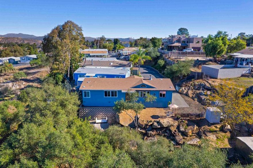Situated at the end of a private road in a gated community, this elevated hilltop retreat offers rare privacy, sweeping city, mountain and valley views, all set in a peaceful, park-like setting. This three bedroom manufactured home is located in a private, gated 27-space community in the highly desirable Crest neighborhood. Positioned at the very end of the road, the property offers exceptional privacy with gated parking for approximately 3 - 4 Vehicles, depending on size. The elevated setting provides breathtaking city, mountain and valley views from the living room, primary bedroom, guest bedroom, and front yard. The exterior offers a serene, park-like atmosphere featuring natural boulders, gentle sloping terrain, and a grove of mature trees just beyond the front yard-ideal for relaxing, enjoying nature, or taking in the expansive views. Inside, the home features an open-concept layout with spacious kitchen, living room, and dining area designed to maximize light and views! Skylights, bay windows, vaulted ceilings and ceiling fans throughout enhance the bright and airy feel. The kitchen includes an island, ample cabinetry, and stainless steel appliances. A separate laundry room includes washer and dryer. French doors lead to a dedicated office with bay windows, offering flexible space for work or guests. The primary suite features vaulted ceilings, generous closet space, and an en-suite bath with a spa tub positioned among tranquil trees, mountains and city views! A wood-burning fireplace anchors the living area, adding warmth and character.  Located in the Crest community, a unique mountain enclave known for its elevated setting, cooler temperatures, and expansive views overlooking the valley and surrounding mountains. Crest offers a quiet, semi-rural atmosphere while remaining conveniently accessible to El Cajon and Interstate 8. The area is characterized by natural landscapes, rock formations, mature trees, and a strong sense of community.  Nearby amenities include Nancy Jane County Park with open green space, picnic areas, and recreational facilities.Local convenience such as a grocery store with wine and liquor, restaurant/cafe are located close by, providing everyday essentials without the need for long travel. Crest is valued for its privacy, scenic beauty, and peaceful lifestyle, making it an appealing alternative to more densely developed neighborhoods while still offering reasonable access to shopping, dining and commuter routes.