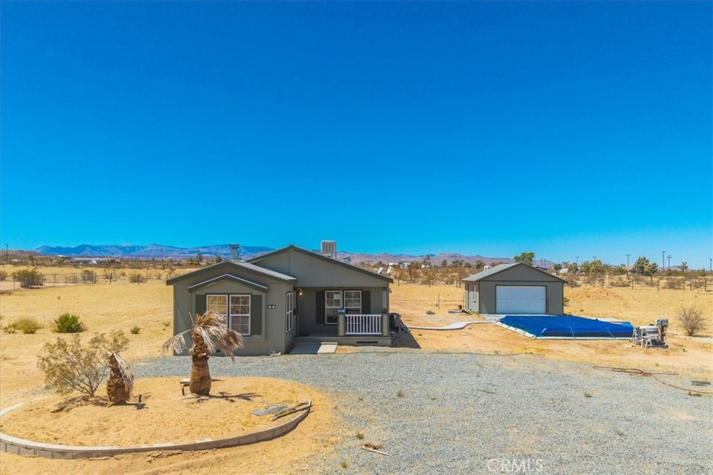 Set on 2.27 acres of open desert land in Landers, this 3 bedroom, 2 bath manufactured home offers space, comfort, and a rare heated POOL for year-round enjoyment. A welcoming wooden front deck sets the tone, inviting you into a large living room with carpeted floors, a cozy fireplace, and ample windows that bring in natural light and showcase sweeping views of the surrounding landscape. The kitchen is spacious and functional, featuring wood-look flooring, warm wood cabinetry, and an open dining area perfect for everyday meals or gatherings. A separate laundry room with outdoor access adds convenience. The home includes two guest bedrooms—each nicely sized and well lit. The guest bathroom is large, with a tub/shower combo and jack-and-jill access to one of the bedrooms, making it ideal for shared living or guests. A second living space provides additional flexibility and includes built-in shelving and a recessed entertainment nook, perfect for creating a media room, home office, or den. The primary bedroom is generously sized and offers a walk-in closet and a private ensuite bath with a walk-in shower and separate garden tub for soaking. Outside, the heated pool offers a rare luxury in the high desert, perfect for enjoying warm days and starry nights. With over two acres of land, there's room to roam, garden, or simply take in the quiet desert beauty. This property combines privacy, comfort, and functionality in one of the most peaceful corners of the Morongo Basin.