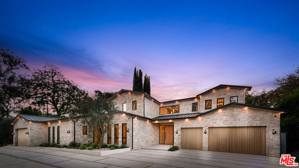 Step into a world of unparalleled design and sophistication in this exclusive private oasis, nestled on over of an acre. This gated Encino estate greets you with a grand motor court, setting the stage for a life of refined elegance and ultimate privacy. Every detail of this compound exudes luxury. The interior is a masterpiece of curated organic finishes, featuring plaster walls and natural stones that seamlessly blend with the soaring high ceilings and fluid indoor-outdoor transitions. The sprawling family room is where comfort meets elegance. This grand space boasts custom built-ins and a stunning fireplace that serves as the room's focal point. Expansive sliding doors reveal breathtaking views of the resort-inspired backyard, creating a seamless connection between indoor elegance and outdoor paradise. The awe-inspiring double island kitchen, along with a secondary chef s kitchen equipped with top-of-the-line appliances, will leave you breathless. The formal dining room is ideal for lavish dinners, where an outdoor fireplace framed by a majestic oak tree provides a stunning backdrop. The primary suite is a sanctuary of luxury, offering not just one, but two private balconies, dual SPA inspired baths, and two massive walk-in closets that promise to satisfy even the most discerning tastes. The executive office adjoins the auto gallery/game room, ensuring that work and play coexist in perfect harmony. Descend to the lower level, where indulgence knows no bounds. Here, a state-of-the-art fitness center with a steam shower, dry sauna, dedicated lap pool and spa awaits. Enjoy blockbuster nights in the luxurious theater, savor your finest vintages in the walk-in wine cellar, and relax in the lounge area complete with a full bar. Each of the en-suite bedrooms offers a private retreat, while additional features such as an elevator, two bars, a media room, two family rooms, two laundry rooms, home automation, and designer light fixtures elevate this estate to the pinnacle of modern living. Step outside to a resort-inspired paradise. An outdoor kitchen, multiple seating areas, and a uniquely designed pool with cascading waterfalls and floating pool beds create an idyllic setting for unforgettable gatherings. A well-appointed guest house provides a luxurious haven for your visitors. This estate is not just a home; it is a testament to where function, elegance, and flawless execution meet, creating a sanctuary that is both majestic and inviting.