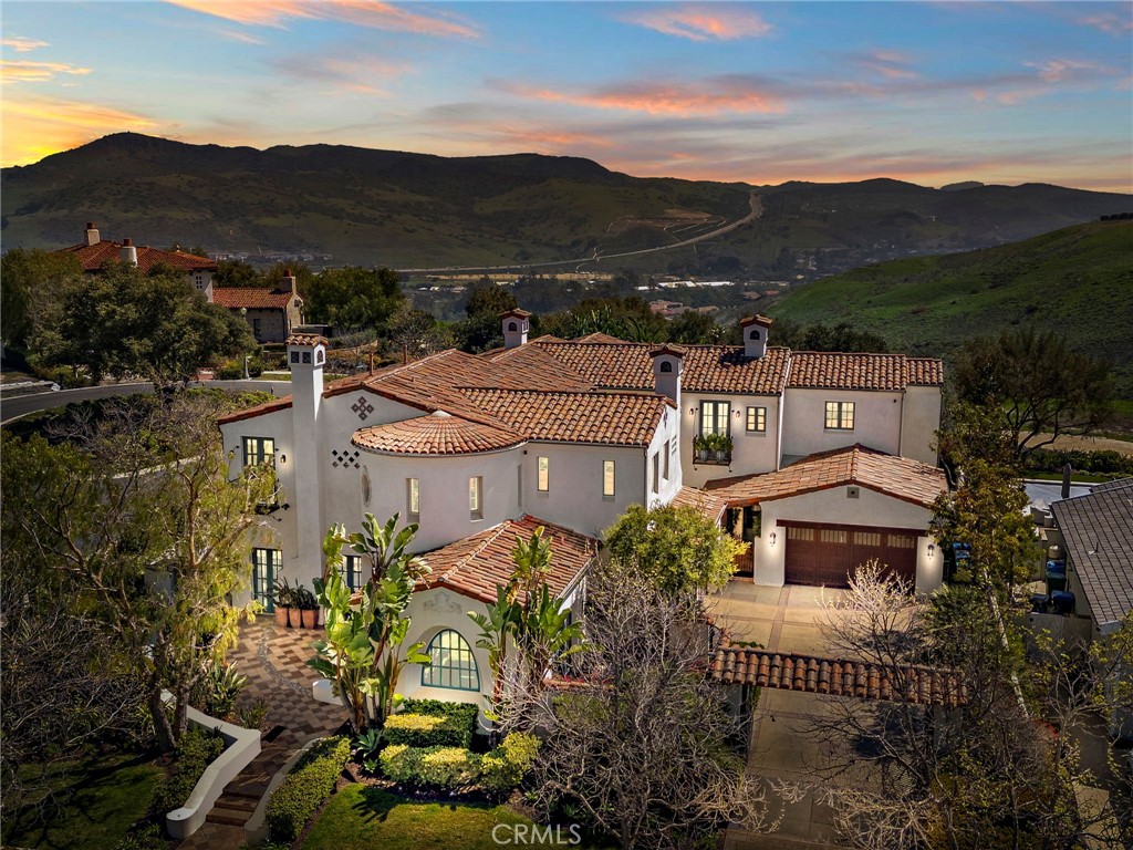 A Timeless Spanish Colonial Estate in Covenant Hills. Reward your success with an extraordinary estate designed to bring generations of joy. Nestled behind the guarded gates of Covenant Hills in Ladera Ranch, 1 Overlook Drive is a masterpiece of Spanish Colonial Revival architecture, offering breathtaking hill and canyon views and grand proportions inside and out. Set on a coveted peninsula lot at the end of a cul-de-sac—with only one direct neighbor and no homes behind—this sprawling property spans nearly 16,000 square feet of meticulously maintained grounds. A gated motor court leads to dual two-car garages, while the backyard is a private oasis, perfect for relaxation and entertaining. Enjoy sun-kissed patios, an open-air fireplace, built-in BBQ with sink, and a stunning pool and spa, all framed by lush landscaping. Nearly every room in the home opens to outdoor spaces, including Juliet balconies and covered patios. Designed by Homer Oatman, this 7,400-square-foot residence boasts five bedrooms and seven baths, blending timeless craftsmanship with modern luxury. A double-height rotunda entry welcomes you to a thoughtfully curated floor plan featuring formal living and dining rooms, a wine cellar, an executive office, and a main-level guest suite. The newly remodeled kitchen is a chef’s dream, showcasing new countertops, custom white cabinetry, an oversized island with seating, a butler’s pantry, and a walk-in pantry. A six-burner Wolf range, coffered ceilings, and a seamless flow into the family room with 16-foot glass pocket doors complete this exceptional space. Throughout the home, exquisite details include triple-stacked exposed ceiling beams, hand-painted tiles from Mexico and Spain, scalloped archways, cast fireplace surrounds, and rich wood flooring. Modern upgrades include Lutron-controlled lighting, Sonos indoor/outdoor audio, an advanced security system with cameras, Life Source water filtration, and picture-framed TVs. The grandeur continues upstairs, where a vaulted-ceiling foyer leads to a view-enhanced loft and generously sized secondary suites. The primary suite is a retreat unto itself, featuring a sitting room with a dramatic fireplace, an enormous custom walk-in closet, and a spa-like bath with dual vanities, a soaking tub, and a spacious shower. Every inch of this residence has been thoughtfully designed and meticulously maintained, creating a sanctuary of elegance, comfort, and enduring beauty. Welcome to a home that defines luxury.