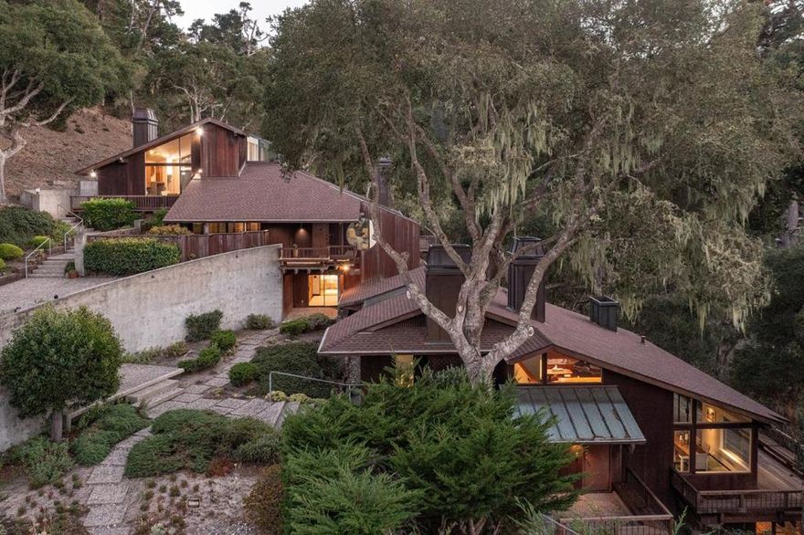 Designed by local acclaimed architect Olof Dahlstrand, this architectural gem blends timeless design with the tranquility of its five-acre Carmel setting. Crafted in redwood and teak, the ~5,777 sq. ft. residence frames sweeping views of Monterey Bay and the surrounding forest through walls of glass and expansive decks. Inside, warm textures and fine materials define every space, including five sculptural concrete fireplaces and custom built-ins throughout. Perfect for entertaining, the home features multiple living areas, including a library and family room, and two full kitchens; one with a commercial-grade Vulcan range and dual Traulsen refrigerators. Four ensuite bedrooms each open to private patios, while the primary suite offers its own fireplace and kitchenette. Additional amenities include a sauna, two laundry rooms, an artist studio with water, and a detached four-car garage. Centrally located within a few minutes' drive into downtown Carmel, Monterey, and all the incredible amenities the Peninsula has to offer, this rare architectural retreat is a place where design, nature, and light exist in perfect harmony.