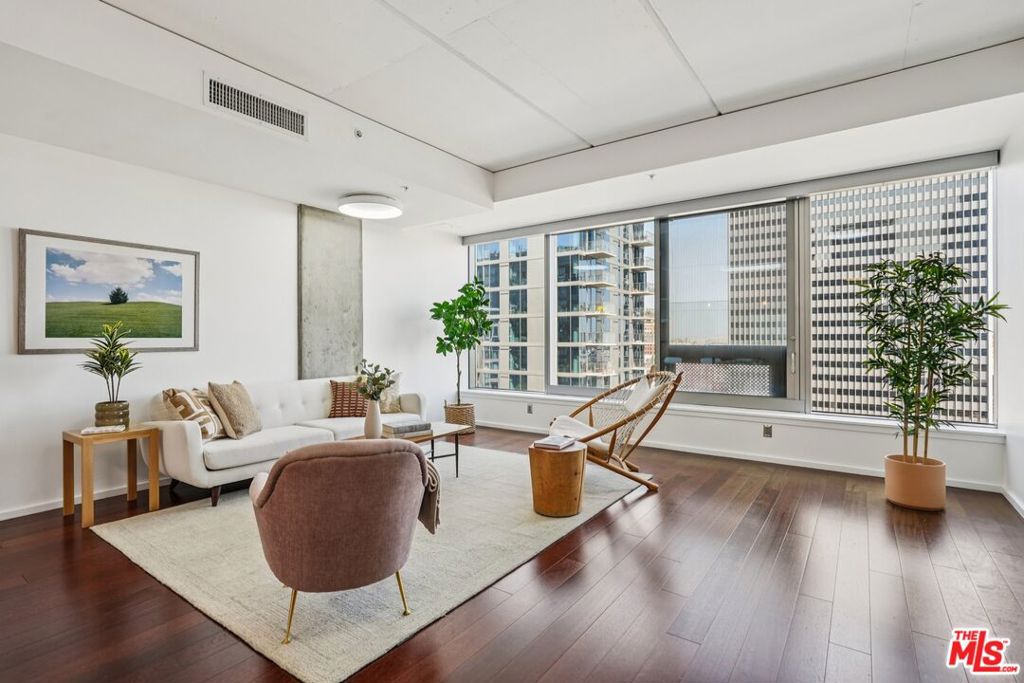 Welcome to EVO South, a LEED-certified architectural standout in Downtown LA's vibrant South Park district. Perched on the 12th floor, Unit #1207 is a bright and spacious 1-bedroom, 1-bath residence that blends contemporary comfort with sleek urban style.The open-concept living space is wrapped in floor-to-ceiling windows, flooding the home with natural light and showcasing sweeping skyline views. Soaring ceilings, a striking concrete column, and wide-plank hardwood floors create a gallery-like feel, while the newly styled interiors bring warmth, texture, and balance to the modern design.The gourmet kitchen features custom European cabinetry, stone countertops, stainless steel appliances, and a large breakfast bar that flows seamlessly into the main living area, ideal for casual dining or entertaining. The bedroom offers privacy with a sliding frosted-glass barn door and built-in wardrobe, while the spa-inspired bath is outfitted with designer fixtures, a deep soaking tub, floating vanity, and linen tower.A separate laundry room includes a stacked LG washer/dryer with added shelving and hanging space for everyday functionality. Living at EVO means access to world-class amenities including a rooftop lounge with panoramic views, a 6th-floor terrace with infinity-edge pool, spa, BBQ stations and outdoor bar, plus a fully equipped fitness center. Residents also enjoy secure entry, front desk concierge, and package handling. One assigned parking space is included.Moments from Whole Foods, LA Live, Crypto.com Arena, and Downtown's best dining and shopping. This is city living at its most refined.