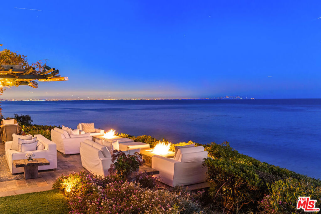 A perfect location, traditional elegance, and contemporary amenities add up to a truly luxurious lifestyle in this spacious, bluff-top Malibu compound. With entertainment industry cachet and sensational views, this ultra-private estate has been perfected for generous indoor-outdoor living and entertaining. At the end of a long, tree-lined drive, the 3-plus acre property comprises magnificent parklike grounds that command extravagant views from Point Dume to the Queen's Necklace, ocean, islands, and sunsets galore. Beautiful interior detailing includes high beamed and coffered ceilings, skylights, large windows, exquisite millwork and built-in cabinets, multiple fireplaces, wide plank hardwood floors, and numerous French doors that open onto expansive ocean-view decks and grounds. The floor plan is open, with easy flow and maximum views. A dramatic double-height foyer leads into the elegant living room, which opens to a deep-covered and heated poolside portico that stretches the full width of the house and offers ample space for lounging, dining, and entertaining. Off the living room is a bright, window-lined family room that extends into a gorgeous wood-wet bar. Also, open to the living room is the formal dining room, with another fireplace and table seating for ten guests. The country kitchen is a professional chef's dream, with two islands, a large pot hanger, Carrera marble countertops, bar seating, Viking, Wolf, and Miele appliances, a walk-in pantry, abundant cabinet space, and a charming breakfast area with a skylight and garden windows. The main floor also features a spacious recreation/game room with skylights and accordion doors to the backyard, an ocean-view office/sunroom with a built-in desk and doors opening onto the portico, plus a huge, two-tier screening room with comfortable couches. Completing the main floor are three en-suite bedrooms and two powder rooms. Upstairs, a fabulous wraparound library mezzanine overlooks the foyer. A hidden door leads to a living room/play area with a built-in desk and walls lined with shelves. Sliding doors reveal an en-suite office that could also serve as a bedroom. There are four beautiful en-suite bedrooms on this level, each opening onto a balcony, including the primary suite, which is a luxurious ocean-view getaway complete with fireplace, over-bed suspended TV, a lavish ocean-view bath, and multiple French doors onto the lounging deck outside. The estate's backyard provides expansive options for recreation and entertaining, with a huge, illuminated "giving tree" at its heart. Features include multiple seating areas, a waterfall swimming pool, Jacuzzi in a heated pergola, a hanging swing, fountains, extensive turf, a covered outdoor living room, and an outdoor kitchen complete with barbecue, pizza oven, counters with bar seating, and private steps leading to the wide sandy beach below. The property's many additional amenities include a double outdoor shower, a fully equipped security system, a security office, an optional on-site security team, a Sonos sound system, driveway parking for ten cars, and optional full-staff services. Extremely warm and welcoming, this classic estate is an achievement in elegance, comfort, and luxury.