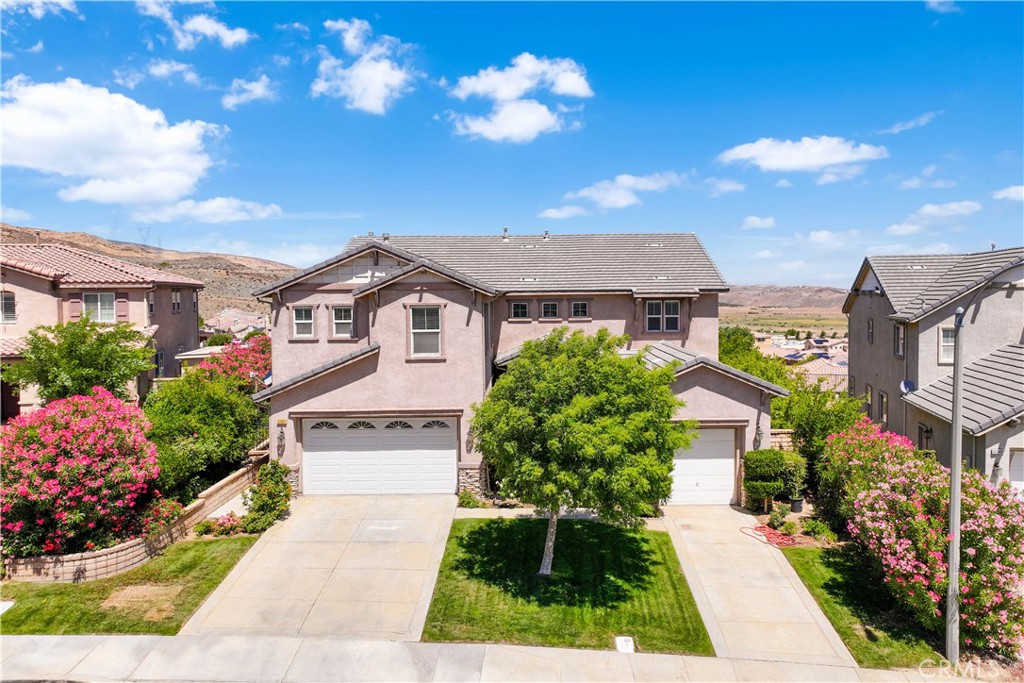 This spacious 5-bedroom home offers comfort, functionality, and stunning views of the AnaVerde Hills and the City of Palmdale. Featuring a highly desirable bedroom and full bathroom downstairs, plus a convenient indoor laundry room with appliances included. Enjoy an open-concept kitchen that flows into the family room complete with a cozy fireplace and built-in entertainment center. The kitchen boasts stainless steel appliances, two kitchen sinks, two ovens, built-in microwave, exhaust fan, refrigerator, and a huge walk-in pantry—a dream for any home chef! Formal dining and living areas, enhanced by window shutters throughout, offer elegant entertaining space. Upstairs, you'll find a spacious loft with fireplace, three additional bedrooms, a full hallway bath, and a luxurious primary suite featuring a private balcony, walk-in closet, spa tub, large shower, and dual vanities. The backyard is perfect for gatherings with a covered patio, concrete slab, and gorgeous hillside views. Plus, a three-car garage with a Tesla charging station adds convenience and value. Don't miss this rare opportunity to own a beautifully upgraded home in one of West Palmdale's most sought-after communities!