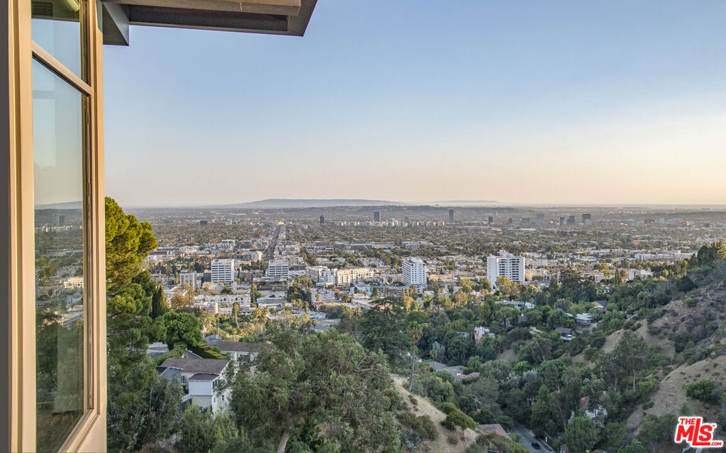 Nestled at the end of a sweeping drive, this gated architectural estate, designed by Glasgow & Lamb, offers a luxurious and secure retreat from the bustling city below. The striking stone and glass architecture seamlessly blends with the surrounding mountains, ocean, Catalina, and city lights views. A long gallery entry leads to the dramatic two-story living room with floor-to-ceiling windows that flood the space with light from the south and west. The adjacent lounge/wine room, formal dining room, and gourmet Miele kitchen flow effortlessly for elegant entertaining. The sleek infinity pool and spa are easily accessible from all public rooms, including the spacious media room with loggia. The generously appointed master suite features a split-level separation from the other en suite bedrooms, each with private terraces. An upstairs corner loft office offers breathtaking 180-degree views. This home boasts state-of-the-art systems, a four-car garage, and a large motor court with parking for eight cars.