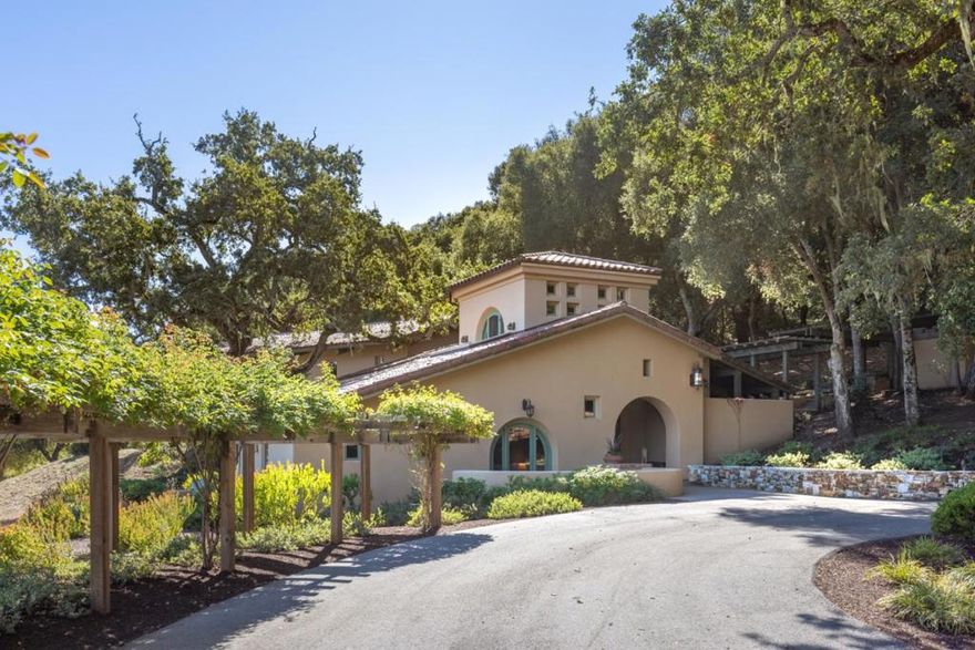 Centrally located in the heart of the Santa Lucia Preserve, this California Spanish Colonial style home embraces clean, contemporary lines with traditional elements like arched doorways and windows, exposed beams and trusses, period-inspired tilework, deep stucco walls and expansive indoor-outdoor living. The house unfolds in a tiered layout, and a grand gallery seamlessly connects the three ensuite bedrooms and library on the West end of the home to the great room and kitchen on the East end, designed to take advantage of the morning sun. A loft above the great room and an office tower are thoughtfully incorporated into the living spaces. A detached 500 sq. ft. workshop is an additional bonus space. Sited against a gently sloping hillside, the home harmonizes with the natural contours of the surrounding trees and landscape. Sweeping views expand beyond the Equestrian Center to the rolling hills of the Santa Lucia Preserve. Within walking distance is the Hacienda, the gym and pool facilities at The Ranch Club and the community hub, The Nest. This timeless residence reflects a thoughtful dialogue between architecture, light, and landscape.