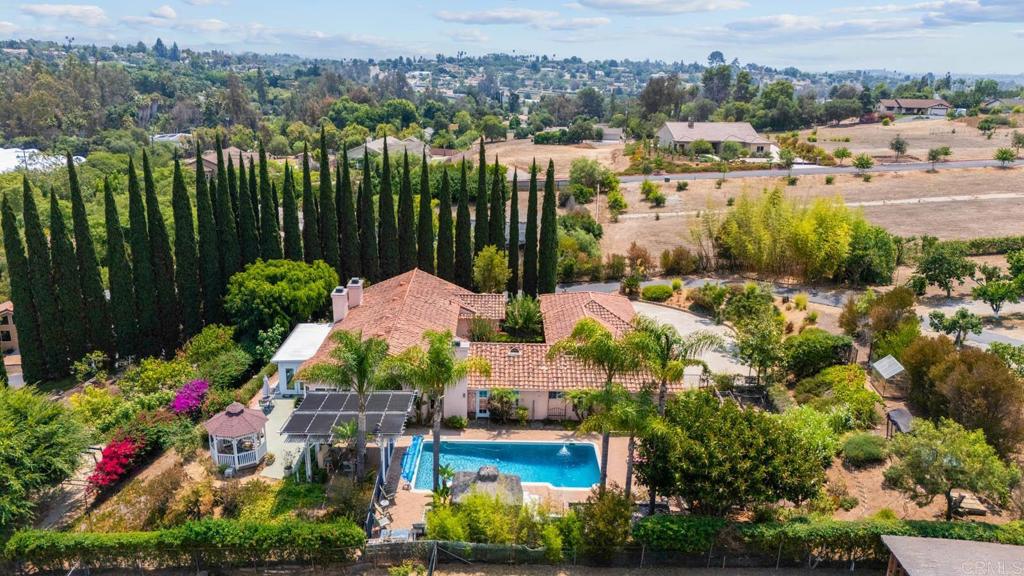 A dramatic gated driveway lined by mature Italian Cypress trees sets the tone for this sprawling single story and enchanting estate. This extensive property offers retreat-like living from the moment you arrive, featuring a welcoming succulent-lined courtyard that leads to grand double doors and soaring vaulted ceilings. Step inside and into the spacious living room with a fireplace that flows into the sunroom, surrounded by walls of windows that flood the home with natural light. These frame the captivating views of Palomar Mountain and overlook the 1.26-acre private oasis—with over 13 fruit trees—blurring the lines between indoor and outdoor living. The kitchen features granite countertops, a center island, stainless steel appliances with Wi-Fi-enabled GE double ovens, a Thermador gas stove with griddle, a roll-out pantry door, ample cabinet space, and a double sink overlooking the backyard pool and adjacent succulent garden. The kitchen effortlessly connects to the dining room, which is warmed by another fireplace and provides direct patio access. The backyard is an escape all its own, featuring a beautiful sparkling pool with a new pool cleaner, an outdoor built-in BBQ area with a grill, burner, prep area, and mini-fridge, and various dining options including a palapa, a covered outdoor dining area, and a gazebo. The orchard is a vibrant mix of mature avocado trees, lemon, orange, mandarin, pineapple guava, olive, fig, and apple trees, as well as blueberries, wild blackberries, dragon fruit, and table grapes. The upper garden boasts a greenhouse and chicken coop, while the lower yard provides tons of room for recreational activities and currently offers a play structure, volleyball area and open space. The primary suite is nestled in a private wing of the home, offering an exclusive sanctuary. This spacious haven features a cozy fireplace, walk-in closet, access door leading to a secluded outdoor patio. The ensuite bathroom offers dual sinks, a soaking tub, a separate shower, and an additional private outdoor access. Three additional bedrooms and one-and-one half bathrooms are found in the opposite wing of the house. This home is equipped with modern conveniences, including a central vacuum system, a wet bar, three gas fireplaces with heat exchange, a three-car garage with 220V wiring for EV charging, all new exterior doors, updated and recently upgraded irrigation system, fresh paint, and dual-zoned air conditioning and heating systems. The Halo whole house water treatment system ensures pure water throughout, and the Texcote exterior paint enhances energy efficiency. A detached artist studio with A/C and heat provides a perfect creative retreat, while the solar panels on a separate covered parking area contribute to energy savings. Experience the tranquility and luxury of Fallbrook living, with close proximity to several wineries including Monserate Winery, parks, hiking trails, dining, shops, and entertainment.