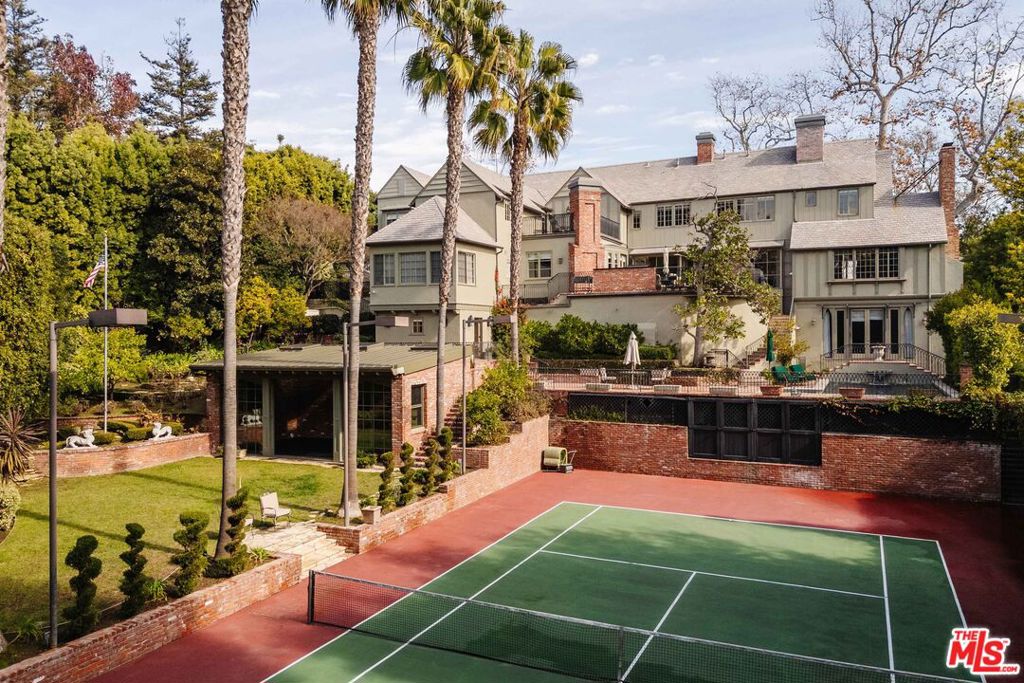 Located on one of Beverly Hills' most prestigious streets, this remarkable tennis estate perfectly blends Old Hollywood glamour with timeless architectural details. Designed in 1933 by world-renowned architect Paul Williams (eight years before redesigning the famed Beverly Hills Hotel), the craftsmanship of this English Country Revival home has been cherished and updated over the years while preserving its architectural provenance. Upon entry, custom millwork, leaded glass, wainscoting, and detailed paneling set the tone in the foyer and formal living room, leading seamlessly to the salon/office/bar and sunroom. Updated in 2010, the modern kitchen features everything a chef could dream of; clad in top appliances from Wolf and Sub-Zero and boasting a large center island. The kitchen is flanked by a den, pantry/butler's pantry, and a large formal dining room. The upper level, accessible via vaulted-beam staircase or elevator, houses four en-suite bedrooms, including the primary wing. This showcase suite, set under massive vaulted ceilings, boasts a fireplace, two large closets, two stately bathrooms, and a balcony. The additional upper bedroom suites, including a guest apartment suite with its own living room, kitchenette, and separate entrance, are all located on a separate wing and are all generously sized. On the lower level, find a 700+ bottle wine cellar, theater with new 4K projector, en-suite office with fireplace, and multiple storage rooms. The backyard may be one of the best in the city, offering a pool/spa, multiple lounge decks overlooking the lit tennis court, firepit, BBQ, grassy yard, gardens, and a new clubhouse/gym. Other amenities include an oversized 4-car garage with a large circular driveway, six-zone HVAC, robust security system, mature landscaping, and more. Old English charm, Hollywood Golden Age motifs, and coveted architecture immaculately combine to achieve true character. It is not often homes of this pedigree and architectural grandeur, especially those designed by Paul Williams, grace the market.