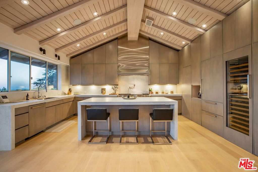 Embodying the essence of warm, earthy sophistication, this designer-done Mid-Century residence is set on over an acre of beautifully landscaped grounds with sweeping views from the Pacific Ocean to the sparkling lights of Downtown Los Angeles. A single-level floor plan flows effortlessly throughout the approximately 5,500SF, 5 bed, 6 bath estate with vaulted wood-clad ceilings and walls of glass that frame vistas extending to Catalina Island. Fleetwood sliders open every room to the outdoors, where a pool, custom pergola with outdoor kitchen, and fire-lit lounge areas create a private retreat for entertaining. Special features include a cedar-lined, climate-controlled wine cave for 2,000 bottles, a wellness enclave with saunas and meditation perch, and gated parking for up to 12 vehicles. Modern upgrades include owned solar and solar pool heating. A full smart-home system, and 7-zone HVAC combine contemporary comfort with timeless design. This is Mid-Century architectural offers a serene sanctuary with distinguished California luxury.