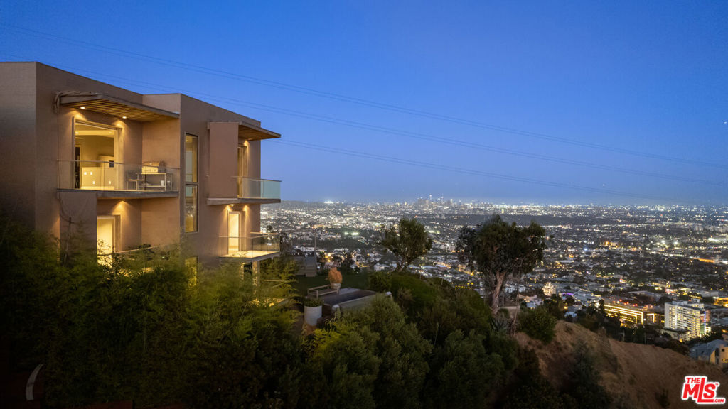 Situated high above the iconic Sunset Strip, this gated architectural masterpiece commands breathtaking jetliner views of the city skyline and the Pacific Ocean beyond. Meticulously designed to harmonize modern sophistication with the surrounding natural beauty, this three-bedroom with an office, five-bathroom residence spans over 3,400 square feet of refined living space. Flooded with natural light, the open-concept interior features disappearing pocket doors that blur the line between indoor and outdoor living, inviting in the shimmering city lights. Nine expansive limestone-clad balconies with covered roofs totaling approximately 700 square feet extend the living space into the open air, ideal for both relaxed lounging and sophisticated entertaining. At the heart of the home, the gourmet kitchen is a showcase of culinary artistry, appointed with top-tier appliances, custom cabinetry, and a generous central island that doubles as a gathering hub. The Primary Suite is a serene retreat, offering sweeping views from its private balcony, a spacious walk-in closet, and a spa-inspired bath with dual vanities and a soaking tub. Thoughtfully designed to embrace the outdoors, the property features a large hot tub, lush landscaping, multiple sitting areas, and a peaceful walking path leading to a scenic overlook. Additional highlights include a gated motor court with parking for up to six vehicles, a media area, detached casita/office, and eco-conscious xeriscape landscaping. Located in the prestigious Viewmont Heights enclave, this rare offering is moments from world-class shopping, dining, and entertainment. The purchase includes 3 APN's (lots) which combine to total ~20,000+ sf of land that potentially allows doubling of the building square footage, providing an exclusive opportunity for a private compound in Hollywood Hills.