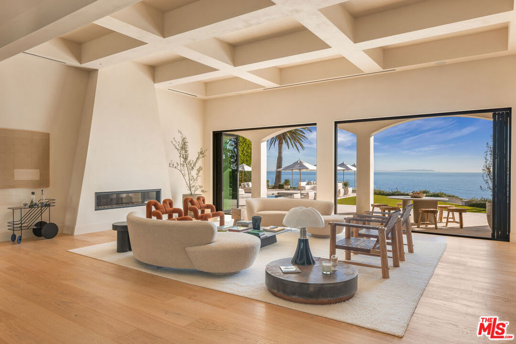 This 2022 estate, reimagined by renowned designer Malgosia Migdal and Fun-Bu Developers, is a single-level masterpiece offering 6,742 square feet of sophisticated living space on 1.55 private acres. Beyond the gates and the long driveway, find lush landscaping , a full tennis court and dual guest houses. Inside the four-bedroom main home, European plaster walls, French white oak floors and exquisite -designer lighting elevates every room. The living area features a box-beam ceiling, a fireplace and a wall of glass that opens to the outdoor entertaining area. The chef's kitchen boasts Miele appliances, leather-finished stone counters and custom rift-cut cabinetry. The primary suite stuns with a cove ceiling, ocean views, a fireplace, dual walk- in closets and a spa-like bath. Additional amenities include a theatre, a stunning pool and spa an outdoor kitchen and pizza oven. A lower-level fire pit and seating area is a serene-space to take in the panoramic ocean views amidst greenery.