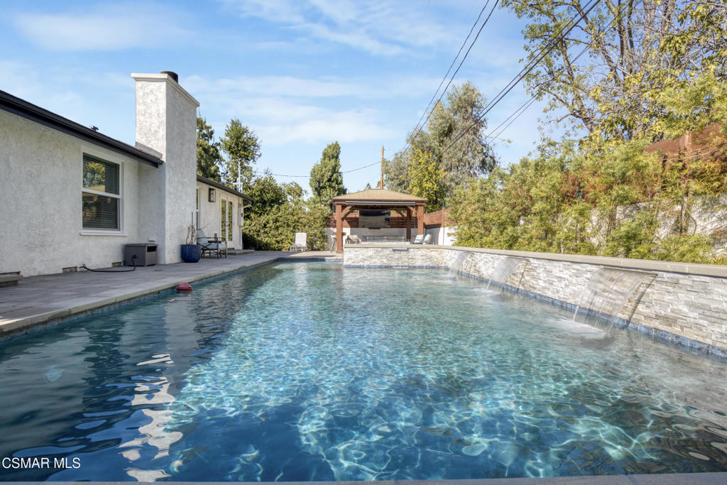 Welcome home to this beautifully updated single-story home in Woodland Hills, with its charming curb appeal. Inside, you'll fall in love with the light-filled, updated interior featuring a sprawling custom kitchen that opens seamlessly to a spacious dining area and large family room, creating a true great-room feel. The kitchen is the heart of the home, beautifully designed with quartz countertops, custom cabinetry, and newer appliances, including a wine fridge, built-in microwave and oven, stainless steel refrigerator, and a newer cooktop perfectly positioned for entertaining. A Kraus Stark stainless steel sink and a large island with a built-in wine rack and additional storage complete this thoughtfully designed space that's as functional as it is inviting.The secondary bedrooms are generously sized, with one offering direct access to the hallway bathroom, creating a perfect mini-suite if desired. The primary bedroom is spacious, featuring ample closet space and private access to the backyard for a peaceful retreat. Both bathrooms have been recently remodeled with new vanities, modern finishes, stylish tile flooring, and walk-in showers with rain shower heads. The primary en-suite showcases an LED mirror and a stunning chevron-tiled shower, creating a luxurious spa-like experience right at home.Step outside to a completely reimagined backyard that is truly an entertainer's paradise. The sparkling saltwater pool, finished in Barbados Blue quartz, is complemented by elegant tiling, an in-ground jacuzzi, waterfalls, and ambient lighting all operated with Aqualink pool equipment. Enjoy evenings around the custom gas fire pit, relax under the gazebo with a custom eating bar, or unwind in the outdoor lounge area. The low-maintenance design with newer pavers makes it as easy to enjoy as it is beautiful to look at.Additional features/updates include a newer HVAC system with updated ducting, water heater, dual-pane windows throughout, a newer roof, a new front door, and flooring that flows seamlessly throughout the home. Every detail has been thoughtfully updated, creating a move-in-ready home that combines modern upgrades with timeless comfort--all in a prime Woodland Hills location, just minutes from Woodlake Elementary, Hale Middle School, and El Camino Real Charter High within the highly sought-after El Camino school district. We can't forget to mention how conveniently located this home is to great shopping and restaurants with The Village, Westfield Topanga Mall, which includes The Topanga Social that brings you some of the trendiest eateries.
