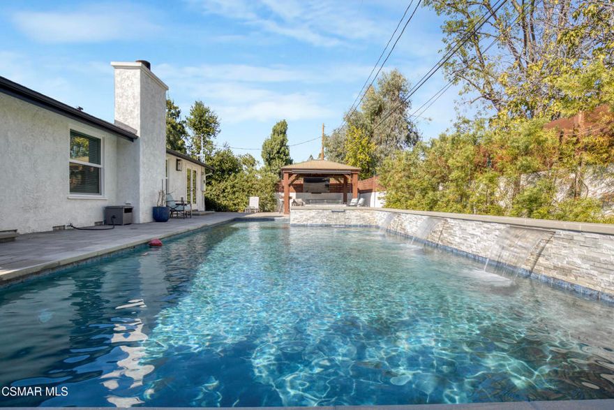 Welcome home to this beautifully updated single-story home in Woodland Hills, with its charming curb appeal. Inside, you'll fall in love with the light-filled, updated interior featuring a sprawling custom kitchen that opens seamlessly to a spacious dining area and large family room, creating a true great-room feel. The kitchen is the heart of the home, beautifully designed with quartz countertops, custom cabinetry, and newer appliances, including a wine fridge, built-in microwave and oven, stainless steel refrigerator, and a newer cooktop perfectly positioned for entertaining. A Kraus Stark stainless steel sink and a large island with a built-in wine rack and additional storage complete this thoughtfully designed space that's as functional as it is inviting.The secondary bedrooms are generously sized, with one offering direct access to the hallway bathroom, creating a perfect mini-suite if desired. The primary bedroom is spacious, featuring ample closet space and private access to the backyard for a peaceful retreat. Both bathrooms have been recently remodeled with new vanities, modern finishes, stylish tile flooring, and walk-in showers with rain shower heads. The primary en-suite showcases an LED mirror and a stunning chevron-tiled shower, creating a luxurious spa-like experience right at home.Step outside to a completely reimagined backyard that is truly an entertainer's paradise. The sparkling saltwater pool, finished in Barbados Blue quartz, is complemented by elegant tiling, an in-ground jacuzzi, waterfalls, and ambient lighting all operated with Aqualink pool equipment. Enjoy evenings around the custom gas fire pit, relax under the gazebo with a custom eating bar, or unwind in the outdoor lounge area. The low-maintenance design with newer pavers makes it as easy to enjoy as it is beautiful to look at.Additional features/updates include a newer HVAC system with updated ducting, water heater, dual-pane windows throughout, a newer roof, a new front door, and flooring that flows seamlessly throughout the home. Every detail has been thoughtfully updated, creating a move-in-ready home that combines modern upgrades with timeless comfort--all in a prime Woodland Hills location, just minutes from Woodlake Elementary, Hale Middle School, and El Camino Real Charter High within the highly sought-after El Camino school district. We can't forget to mention how conveniently located this home is to great shopping and restaurants with The Village, Westfield Topanga Mall, which includes The Topanga Social that brings you some of the trendiest eateries.