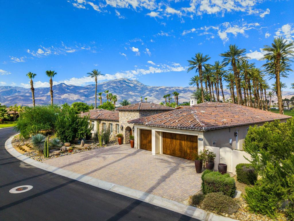 Experience the pinnacle of resort-style country club living at 56985 Village Drive, located in the highly sought-after Palms Country Club. This fully furnished, European Chateau-inspired estate offers 4 bedrooms, 4.5 bathrooms, and a private casita with its own entrance, kitchenette, dining, living, office area, bedroom, and spa-like bathroom with soaking tub, ideal for guests, extended family, or long-term visitors. Every detail of this home has been designed for comfort, elegance, and entertaining. Enter through a monumental private wooden gate into a grand courtyard featuring a central fountain, setting the tone for a residence that blends sophistication with timeless charm. Inside, the formal entryway opens to a formal living room with a billiards table and double-sided fireplace. To the right, a formal dining room, and off the kitchen, the breakfast room which offers expansive windows overlooking the golf course, offering stunning views of the greens, mountains, and palm trees. The chef's kitchen is a culinary dream, featuring a Sub-Zero refrigerator, commercial-grade stainless steel appliances, dual sinks, an eat-up island, and abundant custom built-ins. The residence also includes a large wet bar with wine fridge, perfect for entertaining family and friends. The primary suite serves as a private retreat, with a spa-like bathroom complete with dual vanities, soaking tub, shower, and a generous walk-in closet. Two additional bedrooms provide ample space, while multiple skylights, custom shutters, and ceiling fans throughout the home create an atmosphere of elegance and comfort. A spacious laundry room and 3-car garage, including room for a golf cart, add convenience and practicality. Step outside to a backyard that opens directly onto the golf course, surrounded by mature, lush landscaping. Stone pavers guide you through multiple entertaining areas, including a large covered patio with cathedral ceilings and ceiling fans, and an outdoor built-in BBQ. The pool area is a showstopper, with a large baja shelf, a river-style water feature that wraps around the property, and a waterfall spa. This estate provides seamless access to La Quinta's premier country club amenities, including a lively social calendar, clubhouse, dining, shopping, and nearby equestrian venues, polo fields, and tennis garden. Designed for those who desire luxury, privacy, and an elevated lifestyle, 56985 Village Drive is the ultimate combination of sophistication and desert charm.